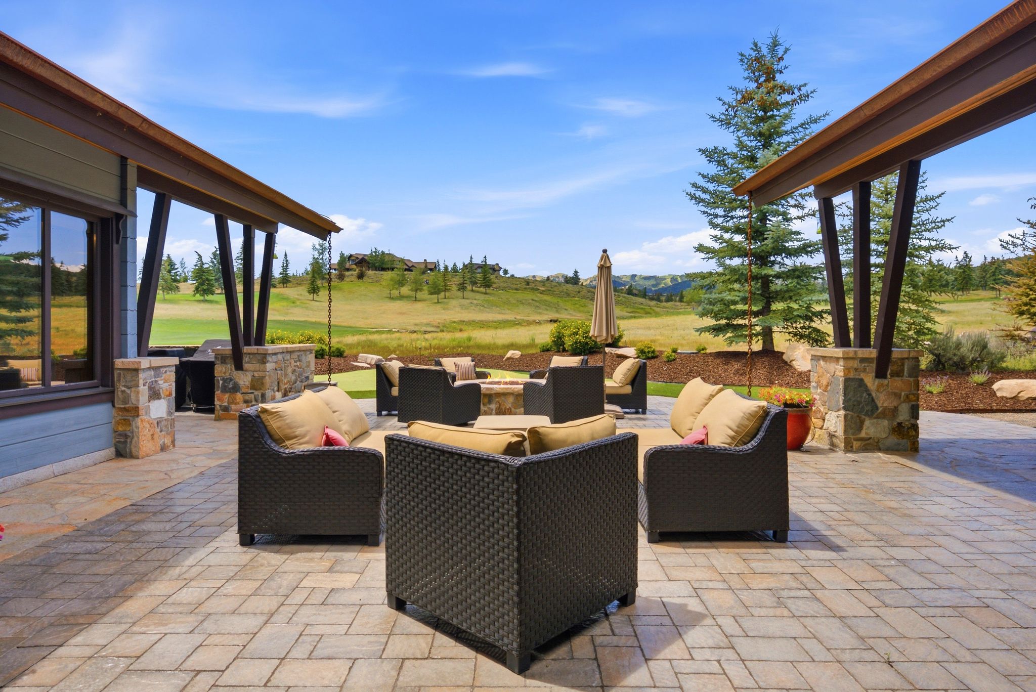 Expansive paver patio featuring a built-in outdoor kitchen with grill, stone fire pit, and covered patio areas with stone pillars
