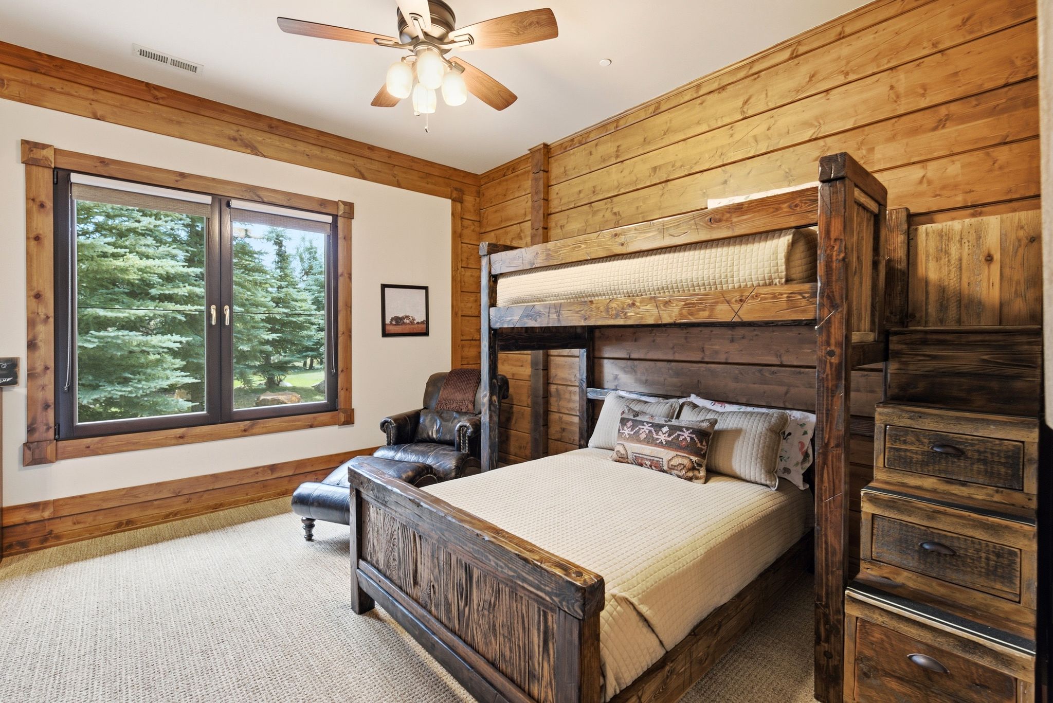 Room featuring a wood-finish bunk bed with integrated storage, a double-paned window with wood trim, wood-paneled walls, and a ceiling fan