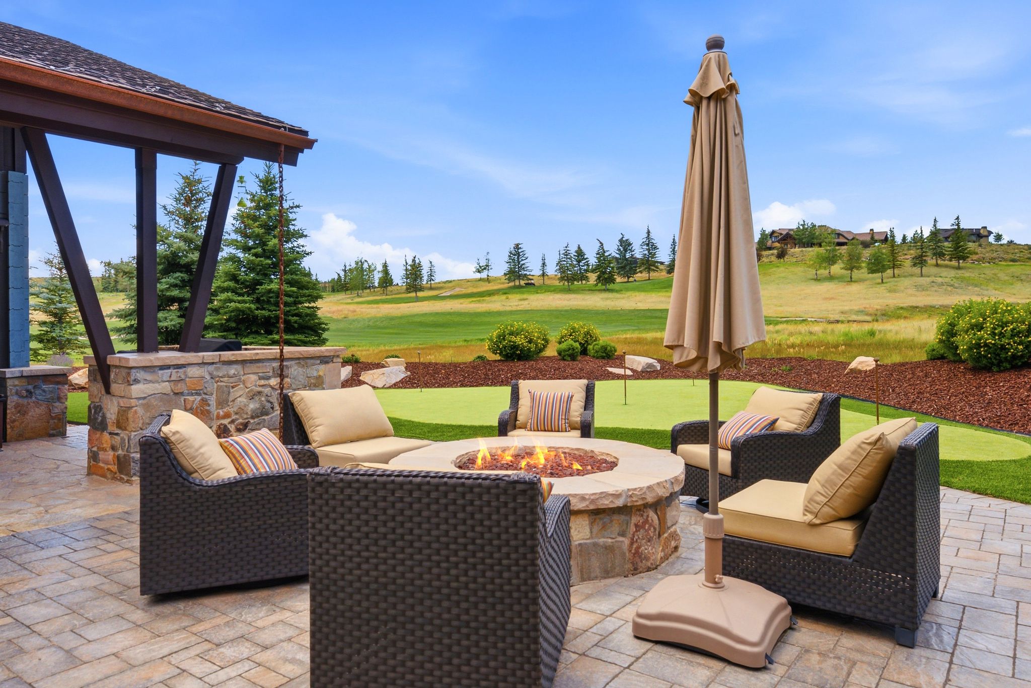 Expansive paver patio with a stone fire pit, built-in stone half-wall, and an overhead structural element