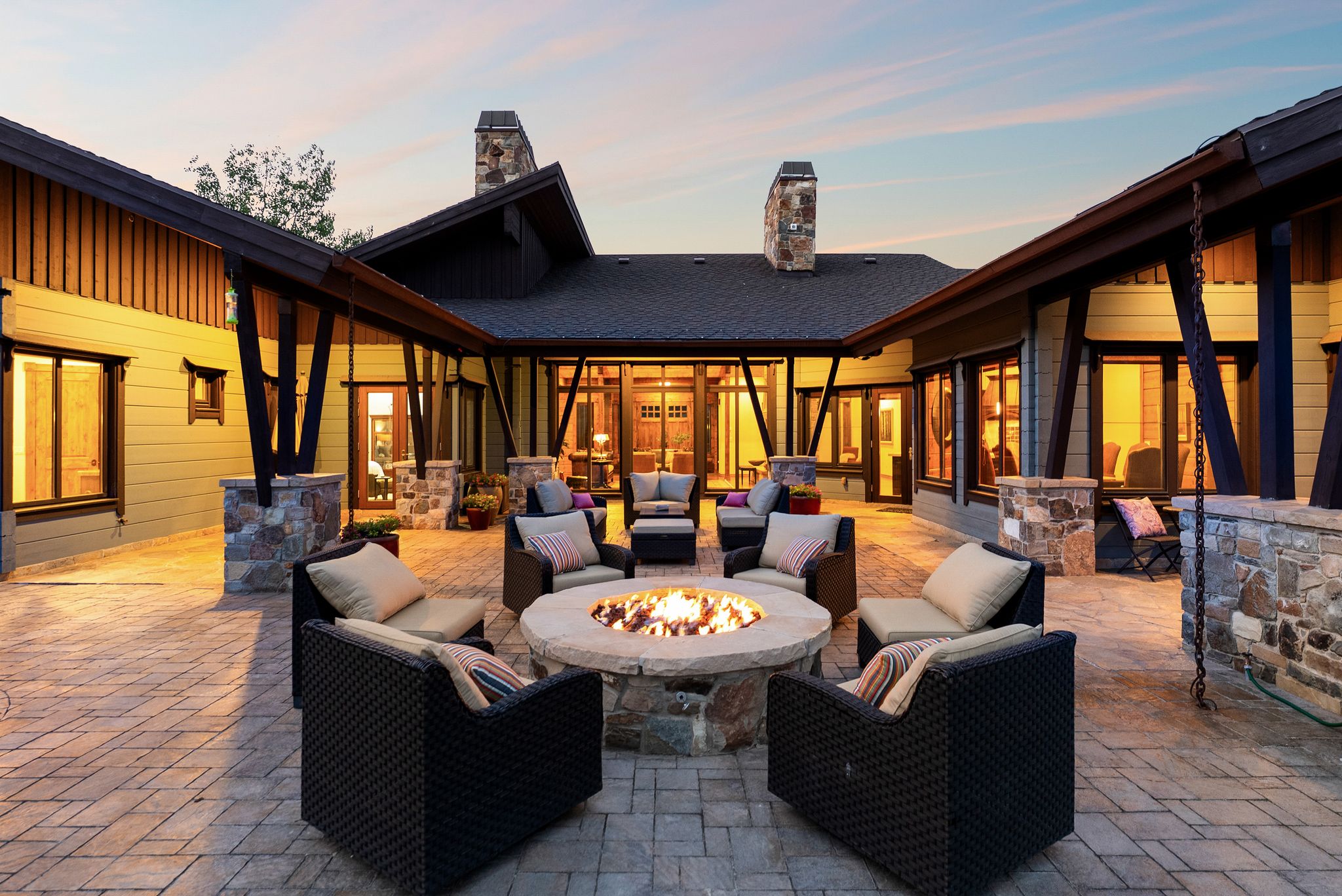 Spacious outdoor patio featuring a stone fire pit, extensive paver flooring, and stacked stone pillars supporting a covered walkway