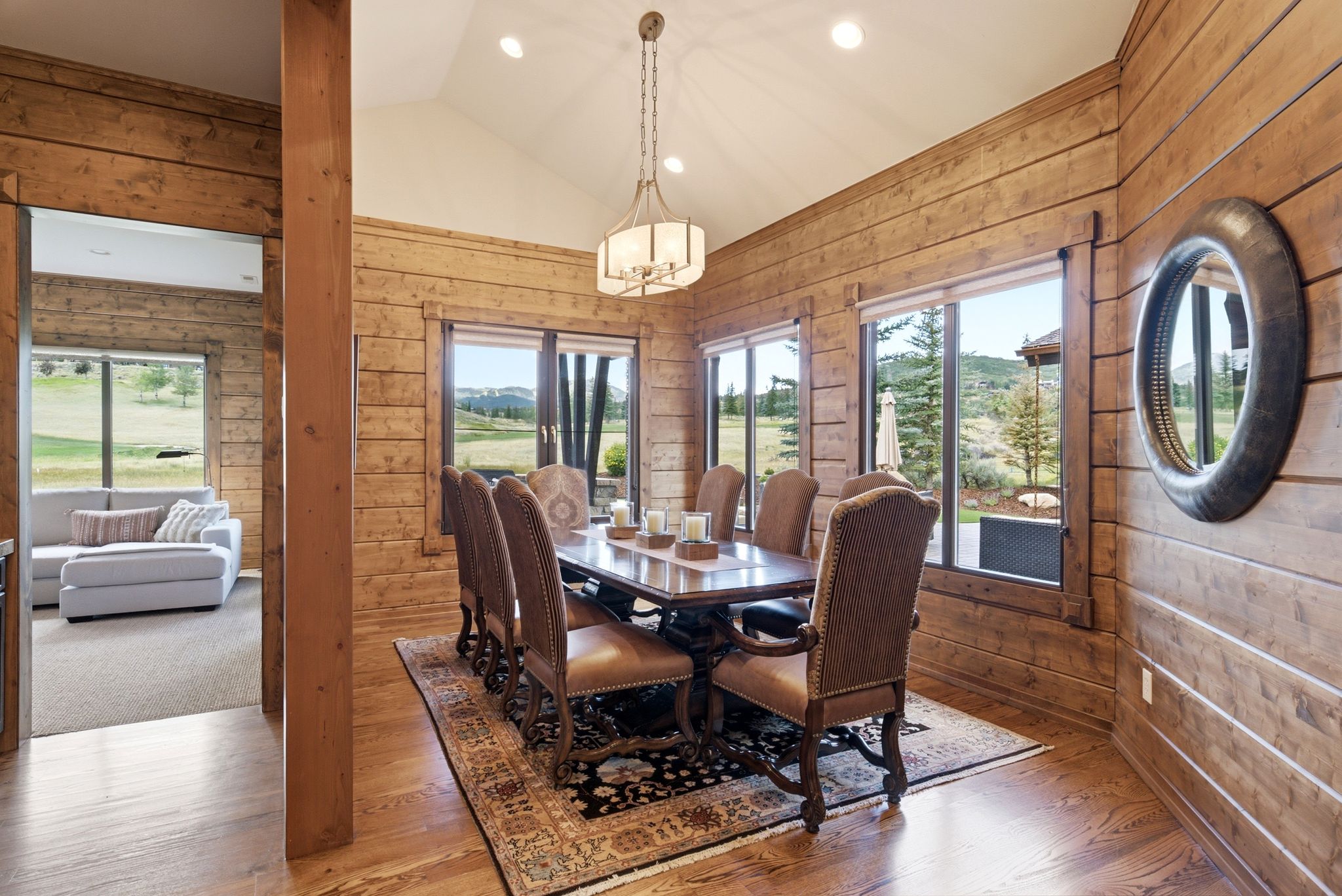 Dining area featuring natural wood plank walls, vaulted ceiling with recessed lighting, and a linear chandelier