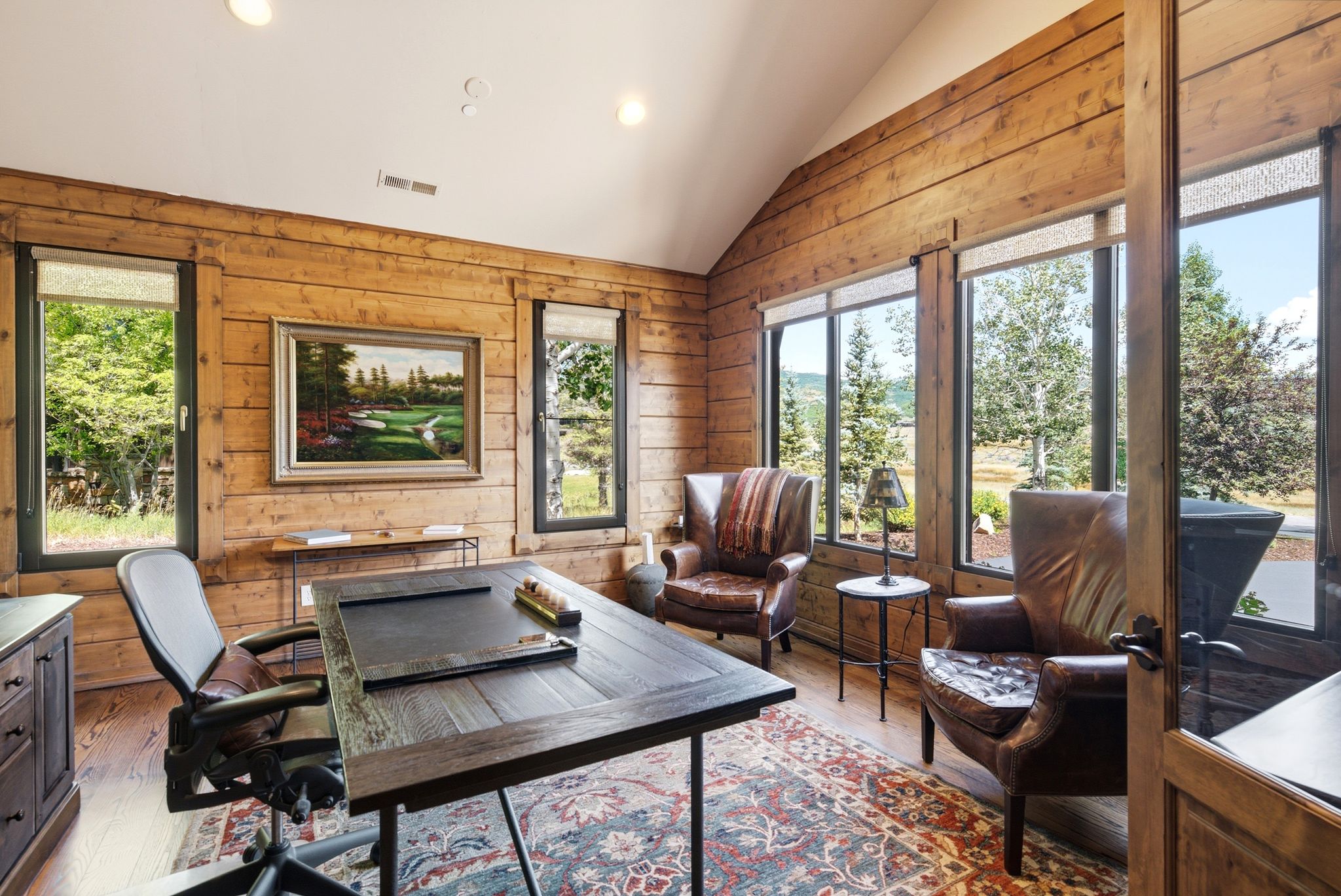 Vaulted wood-paneled room with abundant natural light, showcasing multiple large windows, recessed ceiling lighting, and wood-finish flooring