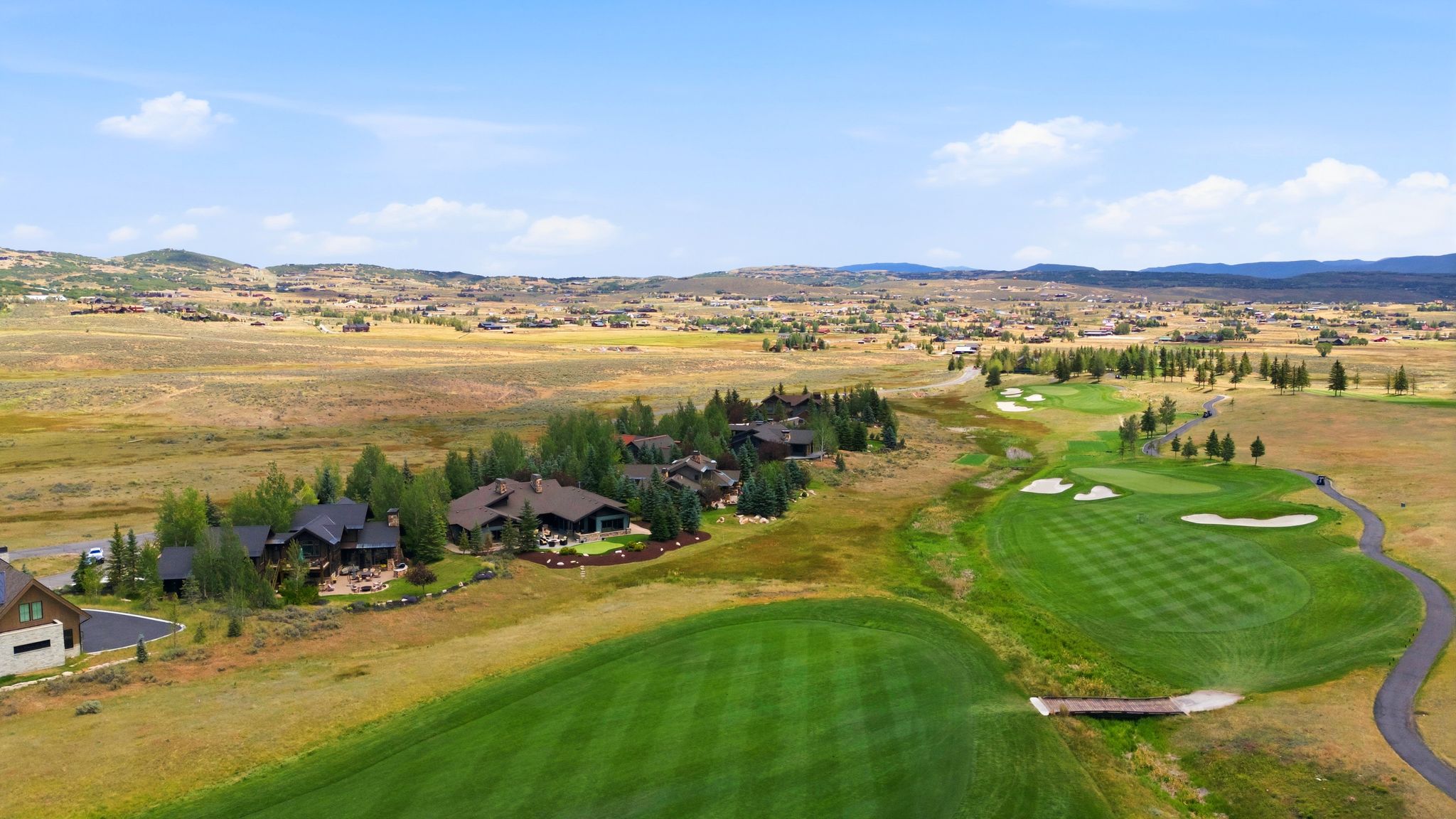 Expansive golf course property featuring manicured greens, a paved cart path, and a rustic wooden bridge