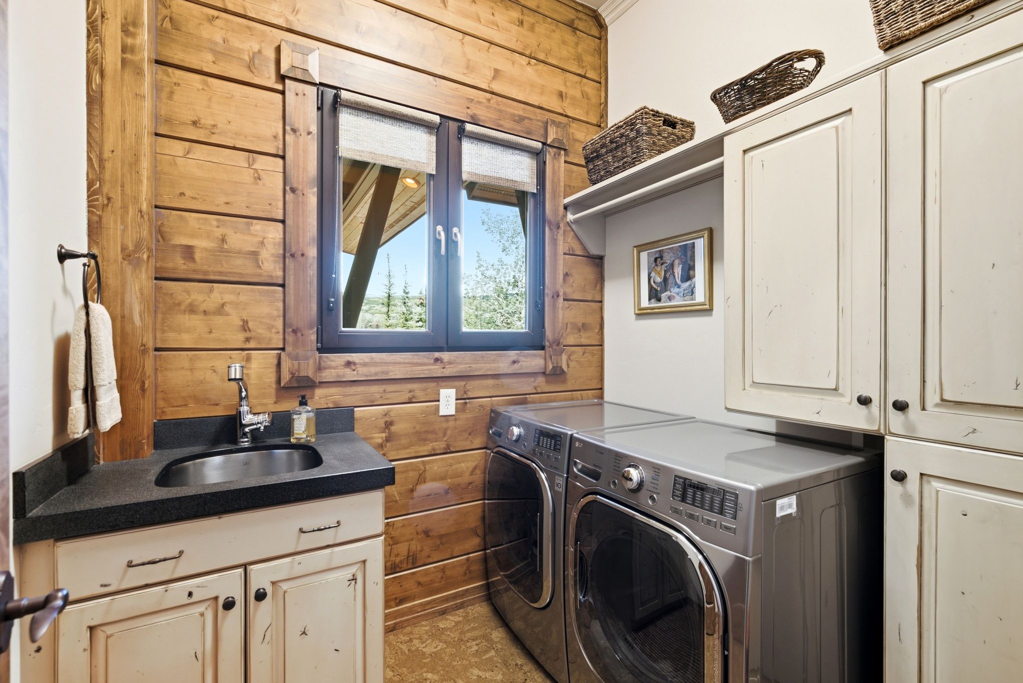 Utility room featuring wood plank walls, a window with exterior views, a vanity with a dark countertop and undermount sink, and extensive cabinetry for storage