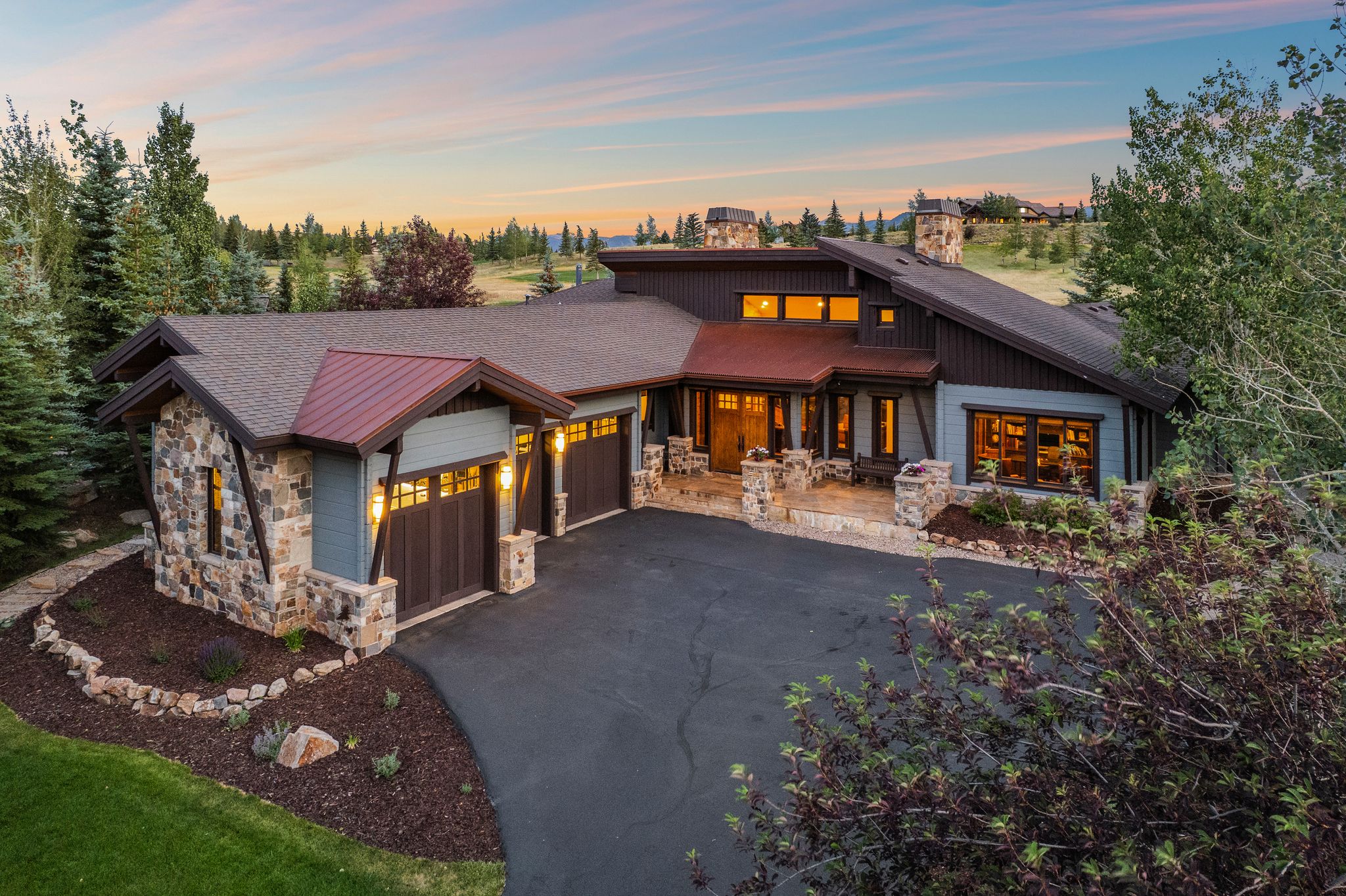 Contemporary home featuring a stone and siding exterior, multiple garage bays with wood-finish doors, a covered entry with stone pillars, and a paved driveway
