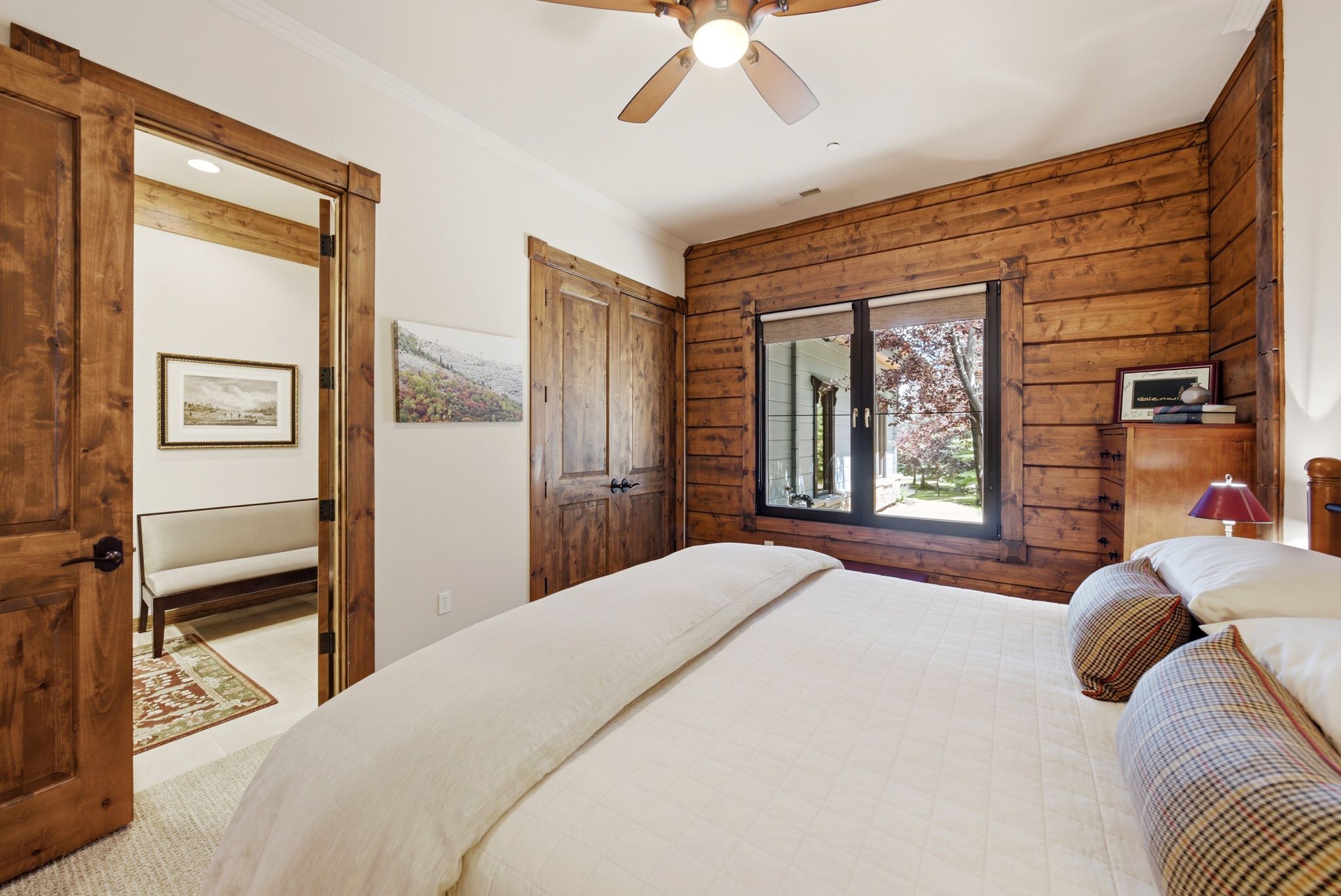 Bedroom featuring a wood-paneled accent wall, a multi-pane window, and a ceiling fan with integrated lighting
