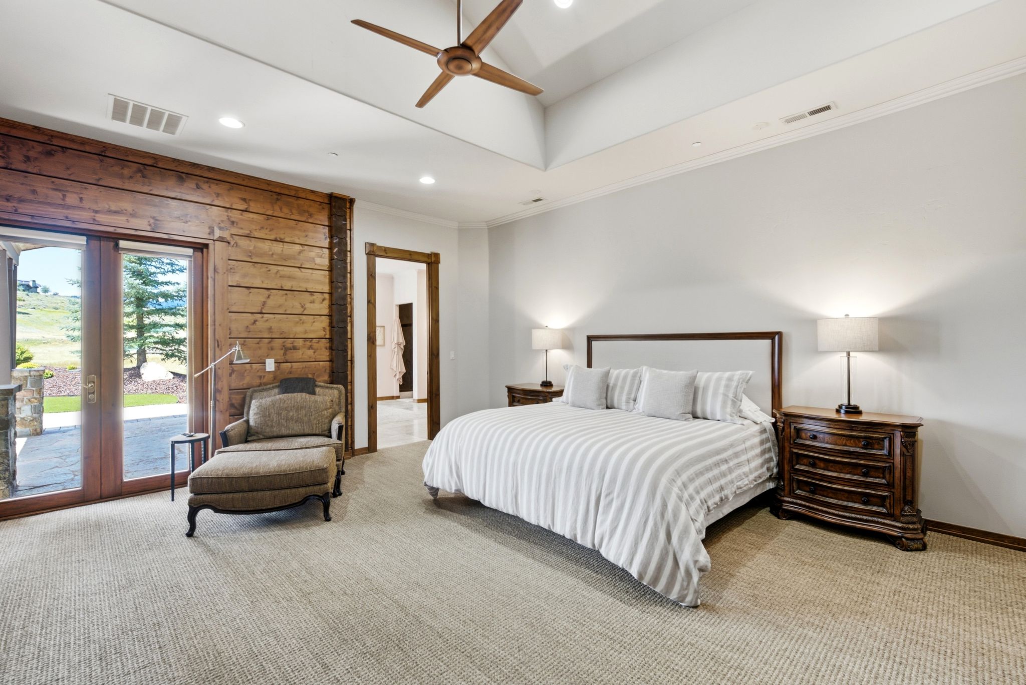 Spacious room featuring a vaulted ceiling with a wood-blade ceiling fan, light-colored carpet flooring, and a prominent wood accent wall