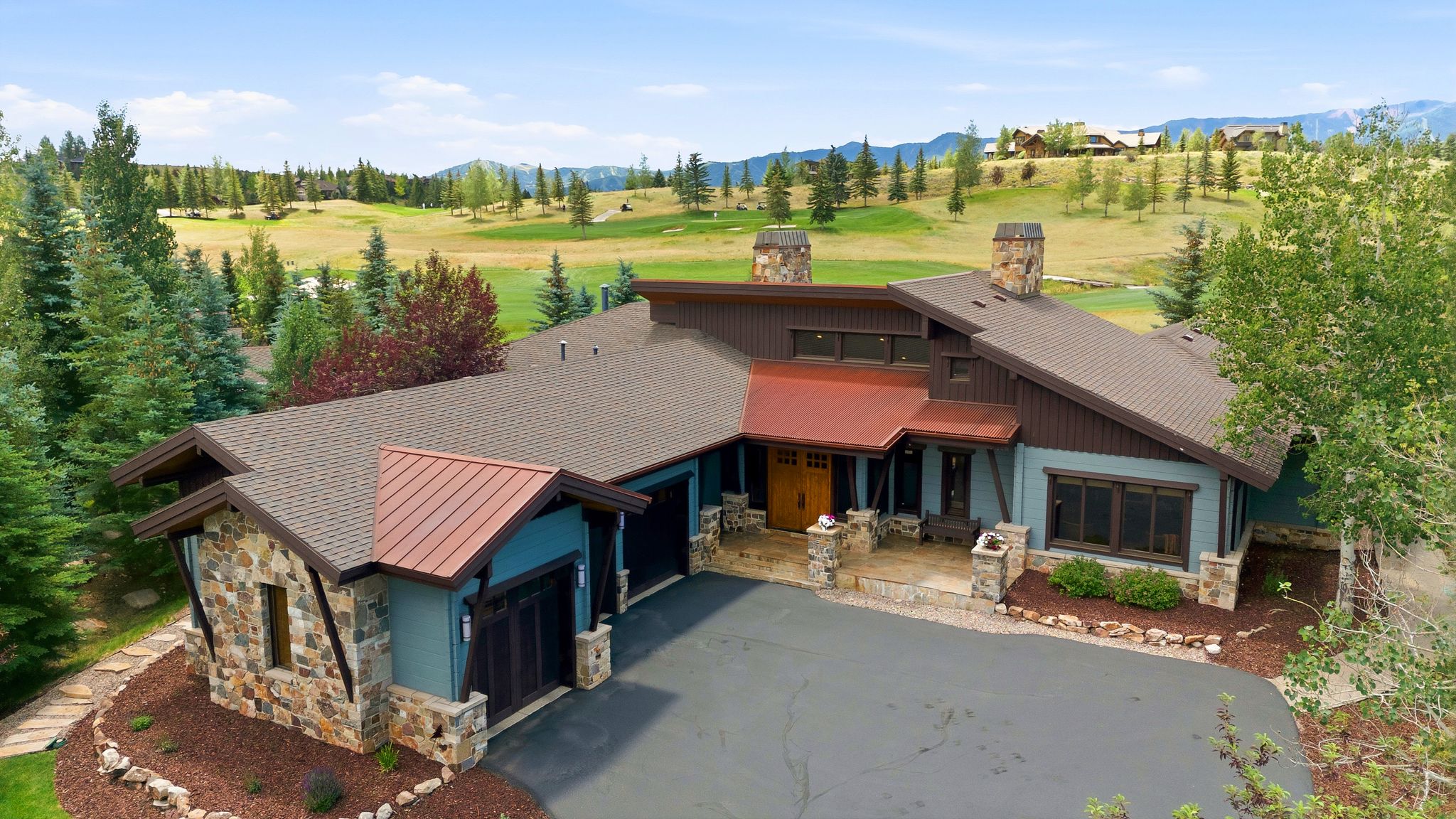 Rustic modern residence featuring stone and siding exterior, multiple rooflines with copper accents, an attached multi-car garage, and a paved driveway