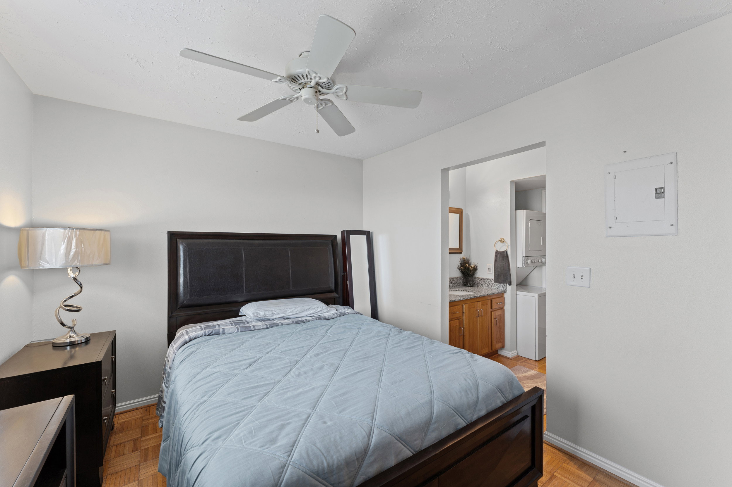 Bedroom featuring wood-finish flooring, a ceiling fan, and access to an adjacent utility area with a stacked appliance