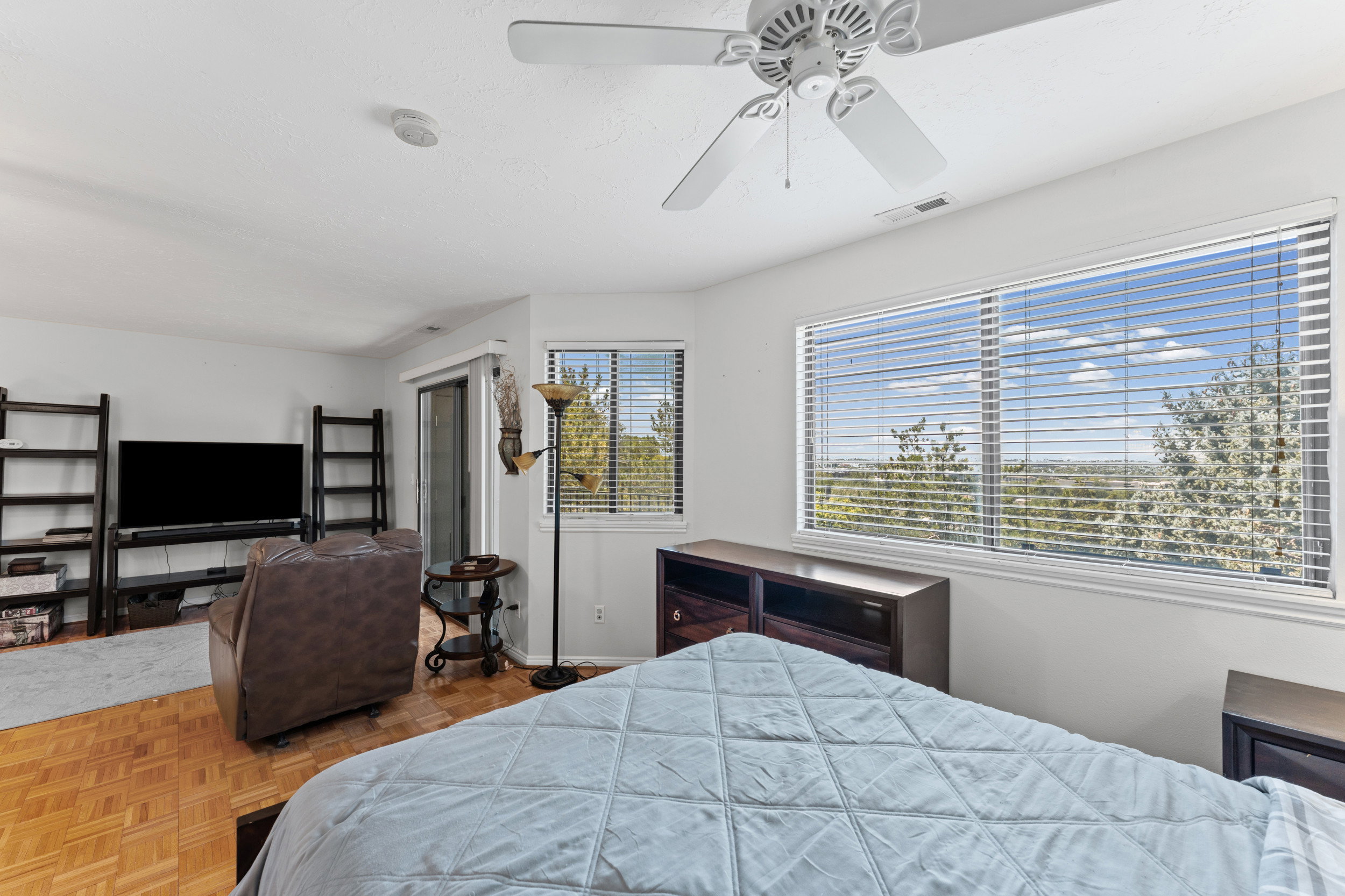 Bright room featuring expansive windows with white blinds, wood-finish parquet flooring, and a ceiling fan