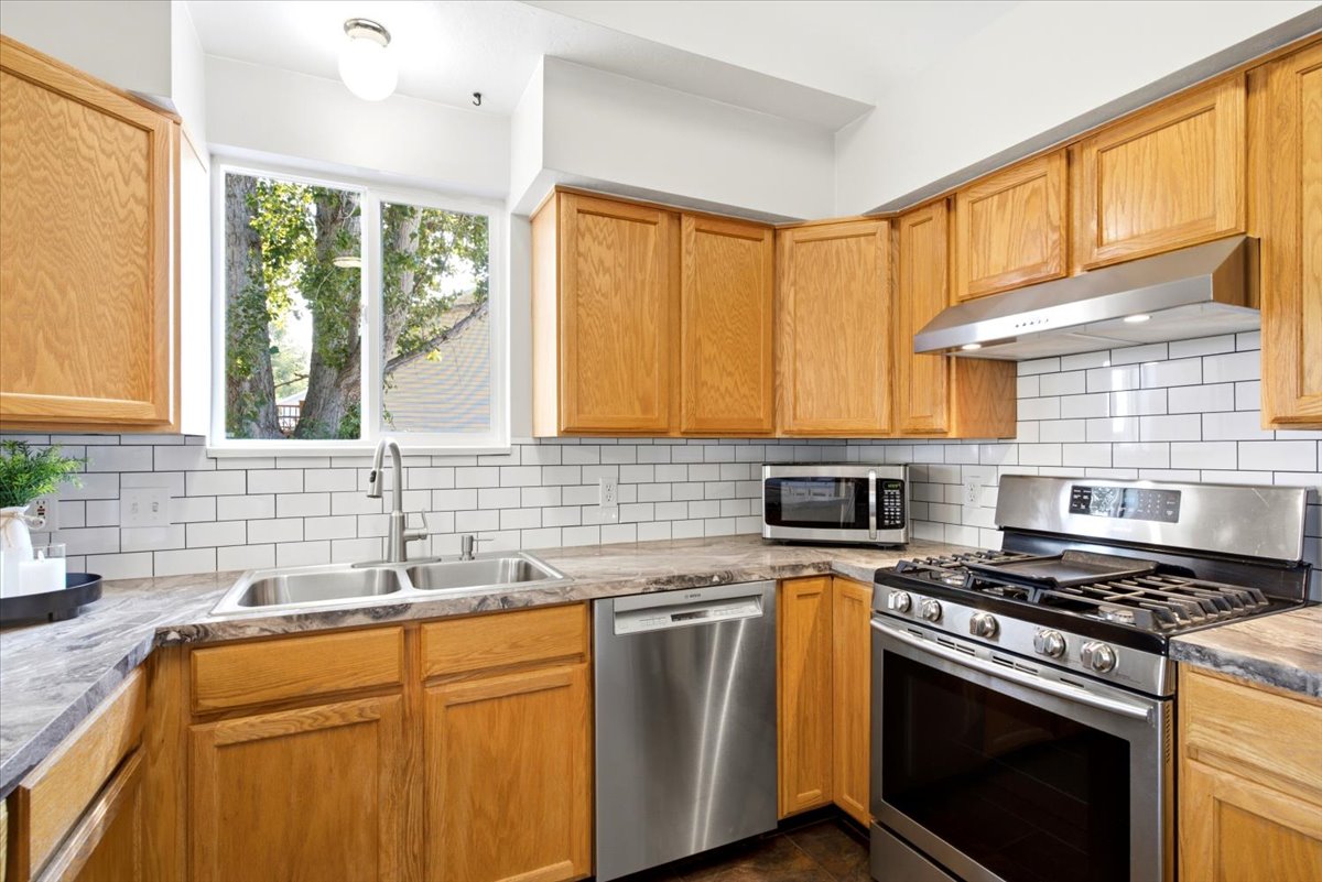 Kitchen featuring wood cabinetry, white subway tile backsplash, stainless steel appliances, a double basin sink, and a window