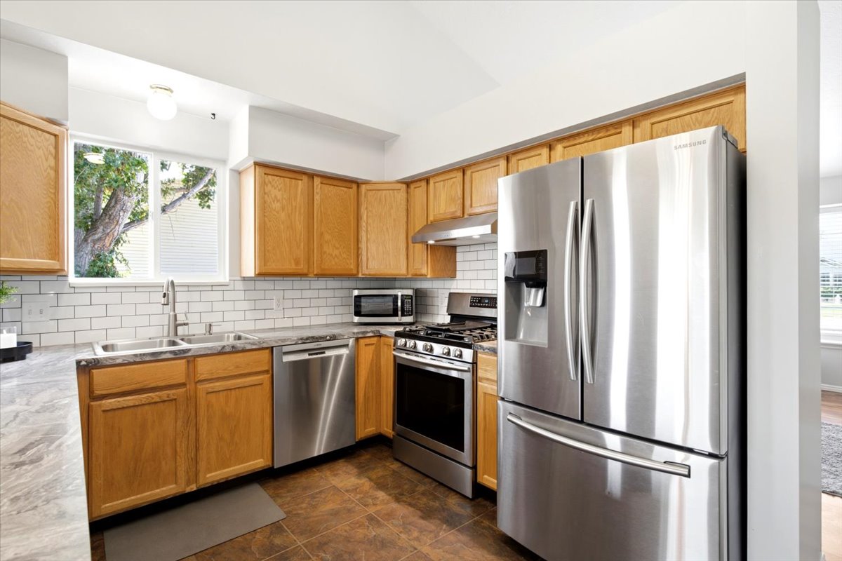 Kitchen featuring stainless steel appliances, wood cabinetry, a subway tile backsplash, and a double basin sink