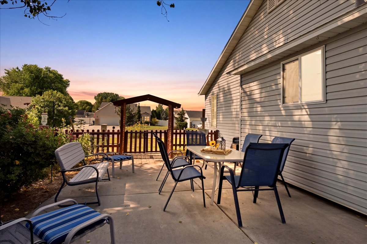 Exterior concrete patio featuring a wooden fence with an arched gate, surrounded by mature landscaping and a residential backdrop