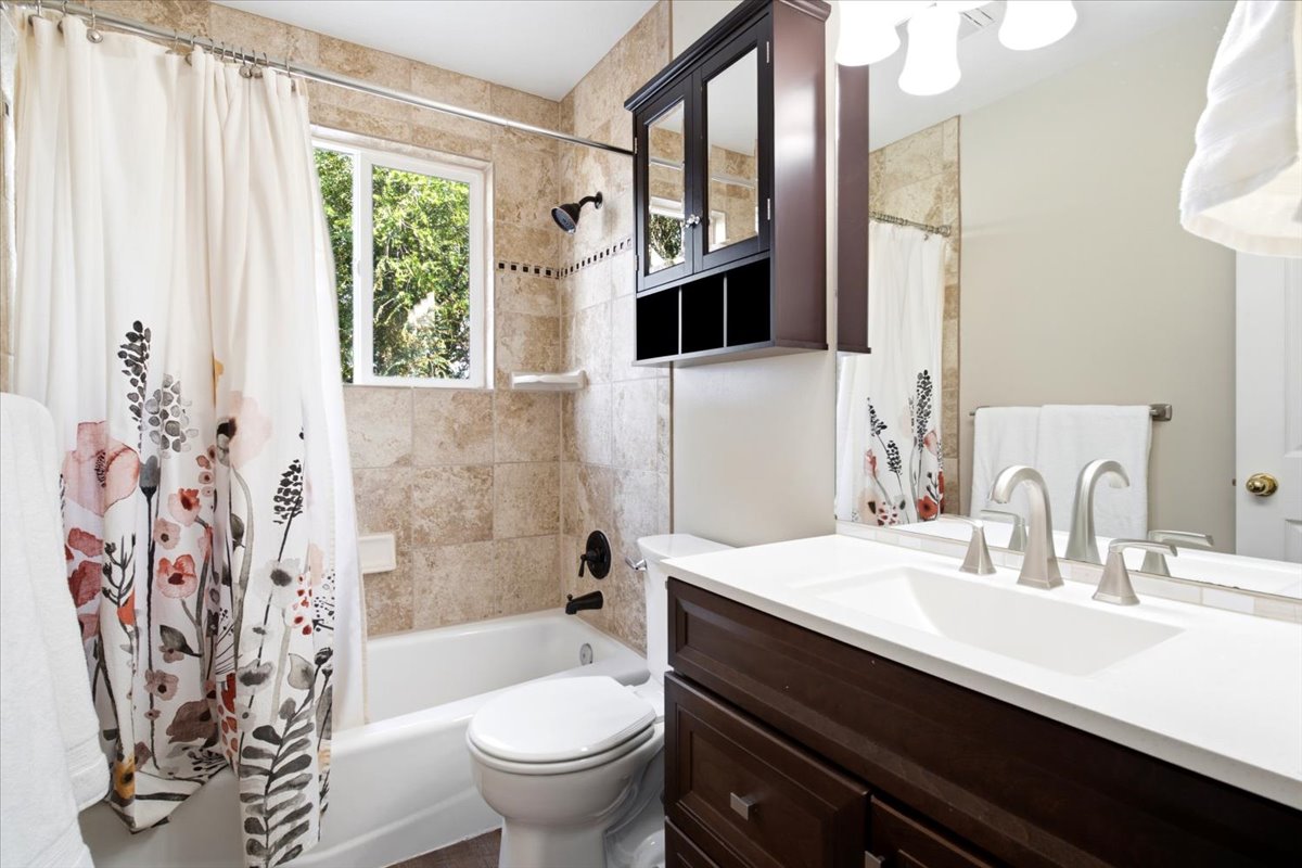 Full bathroom featuring a single vanity with a white countertop and dark wood cabinetry, a built-in shower/tub combination with tile surround, and a wall-mounted medicine cabinet