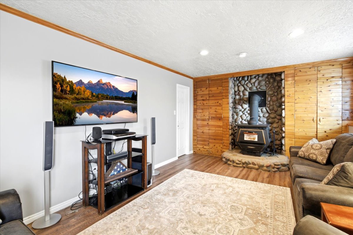 Living area featuring a stone fireplace with a wood-burning stove, wood-finish flooring, recessed lighting, and wood paneling on one wall