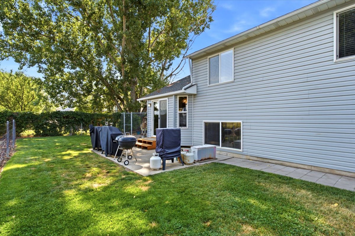 Expansive lawn area featuring a concrete patio, a small wooden deck, and mature perimeter trees