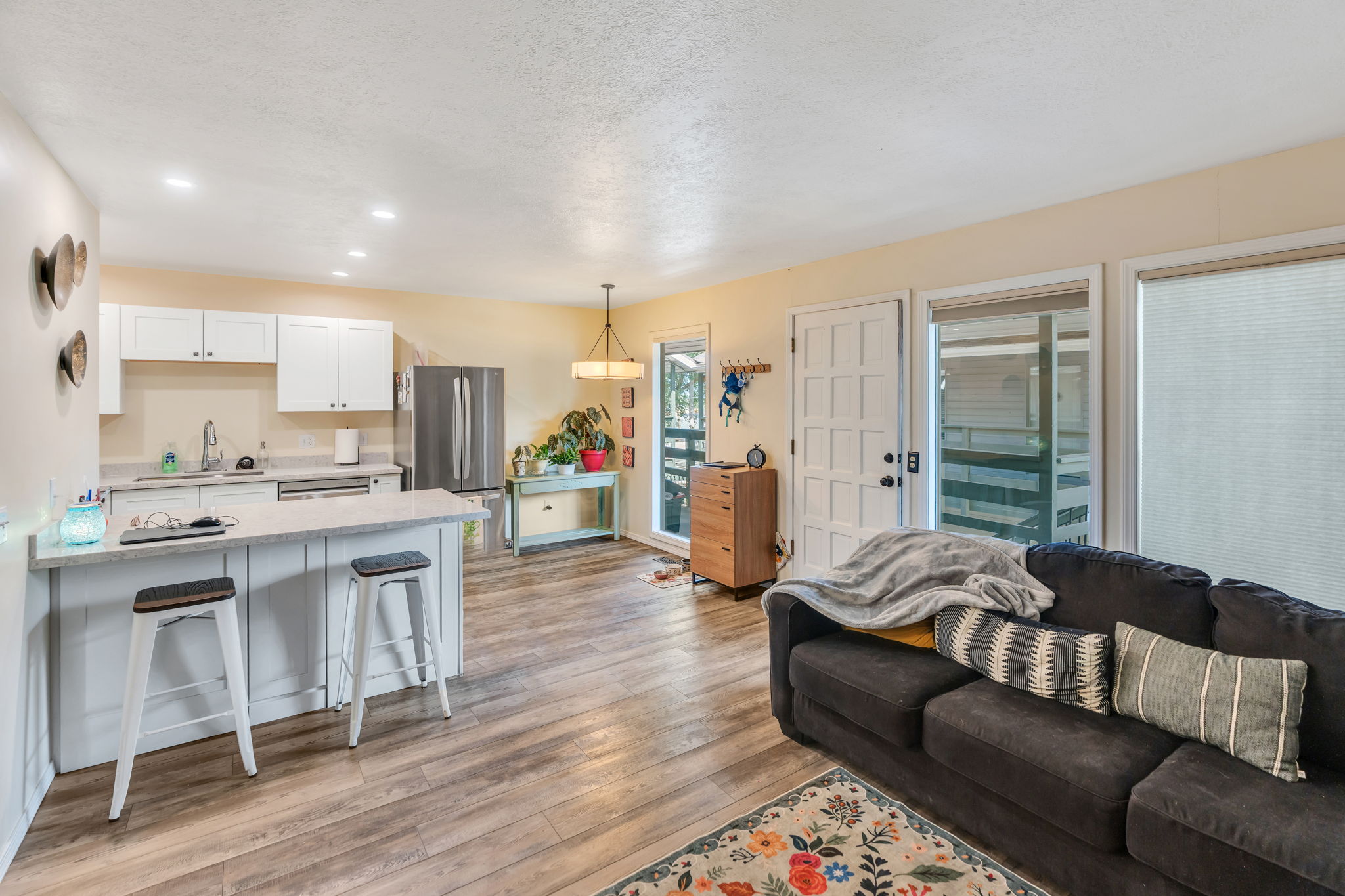 Open-concept living space featuring wood-finish flooring, a kitchen island with seating, white cabinetry, stainless steel appliances, and large windows