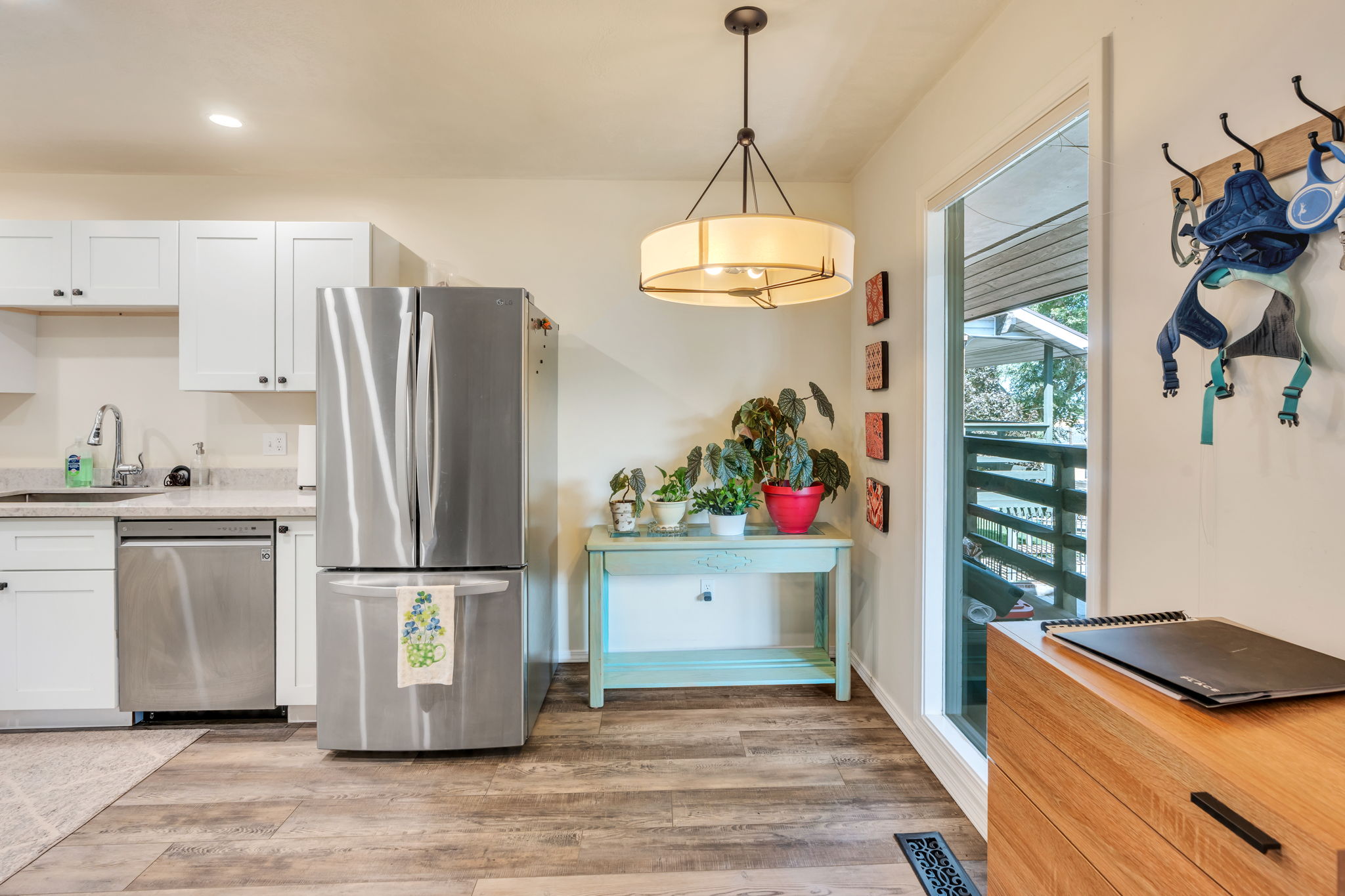 Kitchen featuring white shaker cabinetry, stainless steel appliances, light-toned countertops, wood-finish flooring, and a modern pendant light fixture