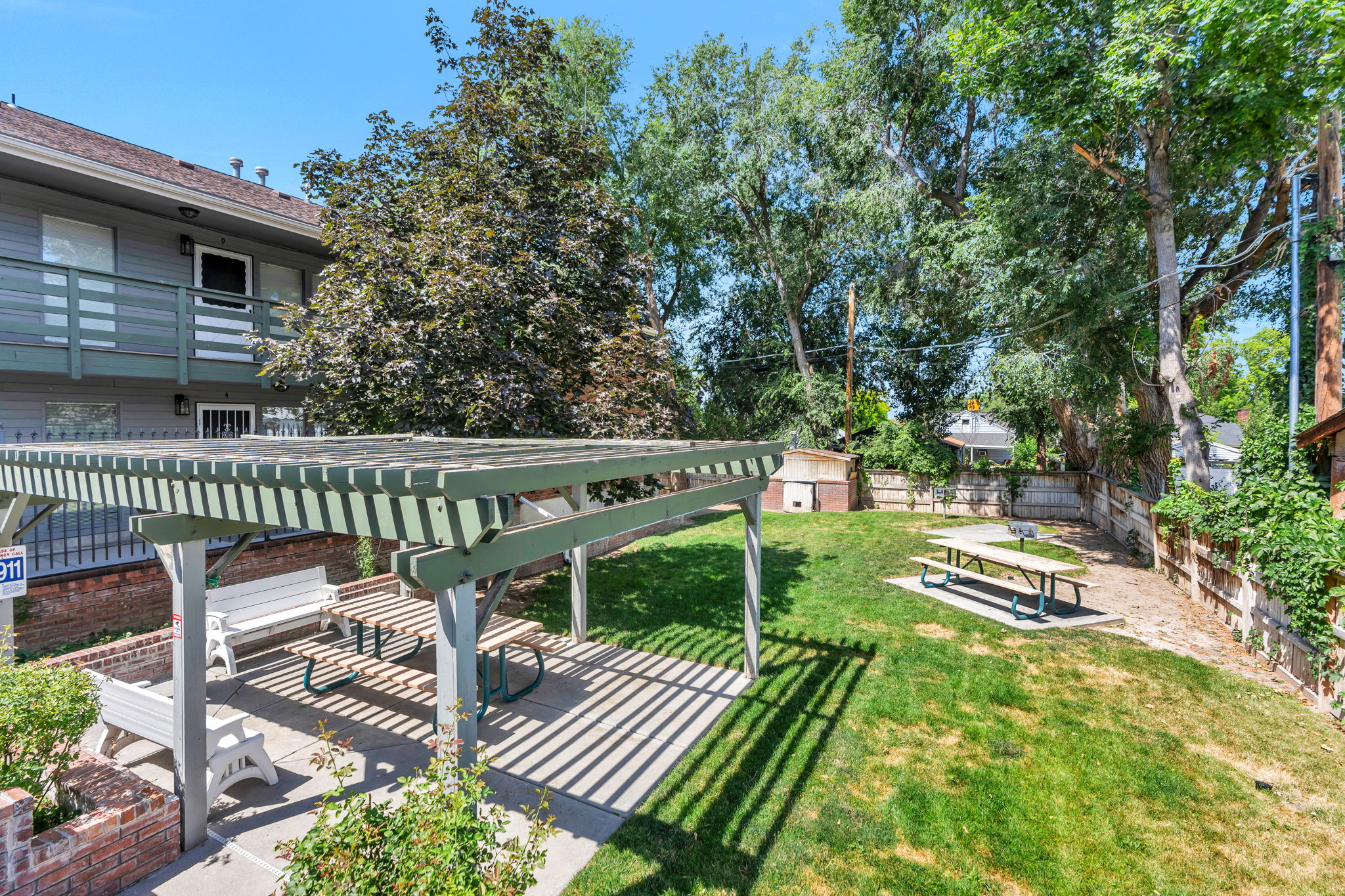 Expansive outdoor space featuring a pergola-covered patio, mature trees, a manicured lawn, and a picnic table area