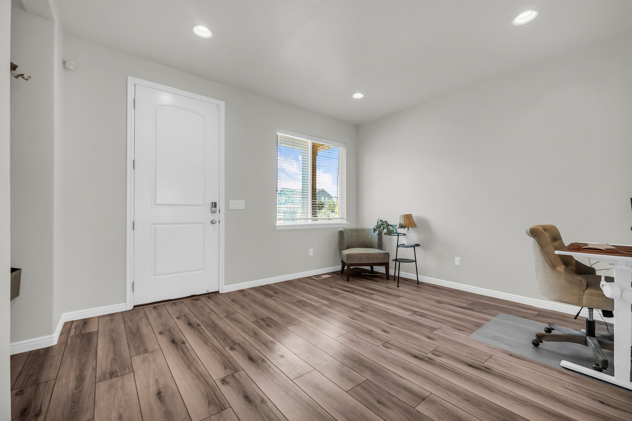 Spacious room featuring wood-finish flooring, recessed lighting, and a white paneled entry door