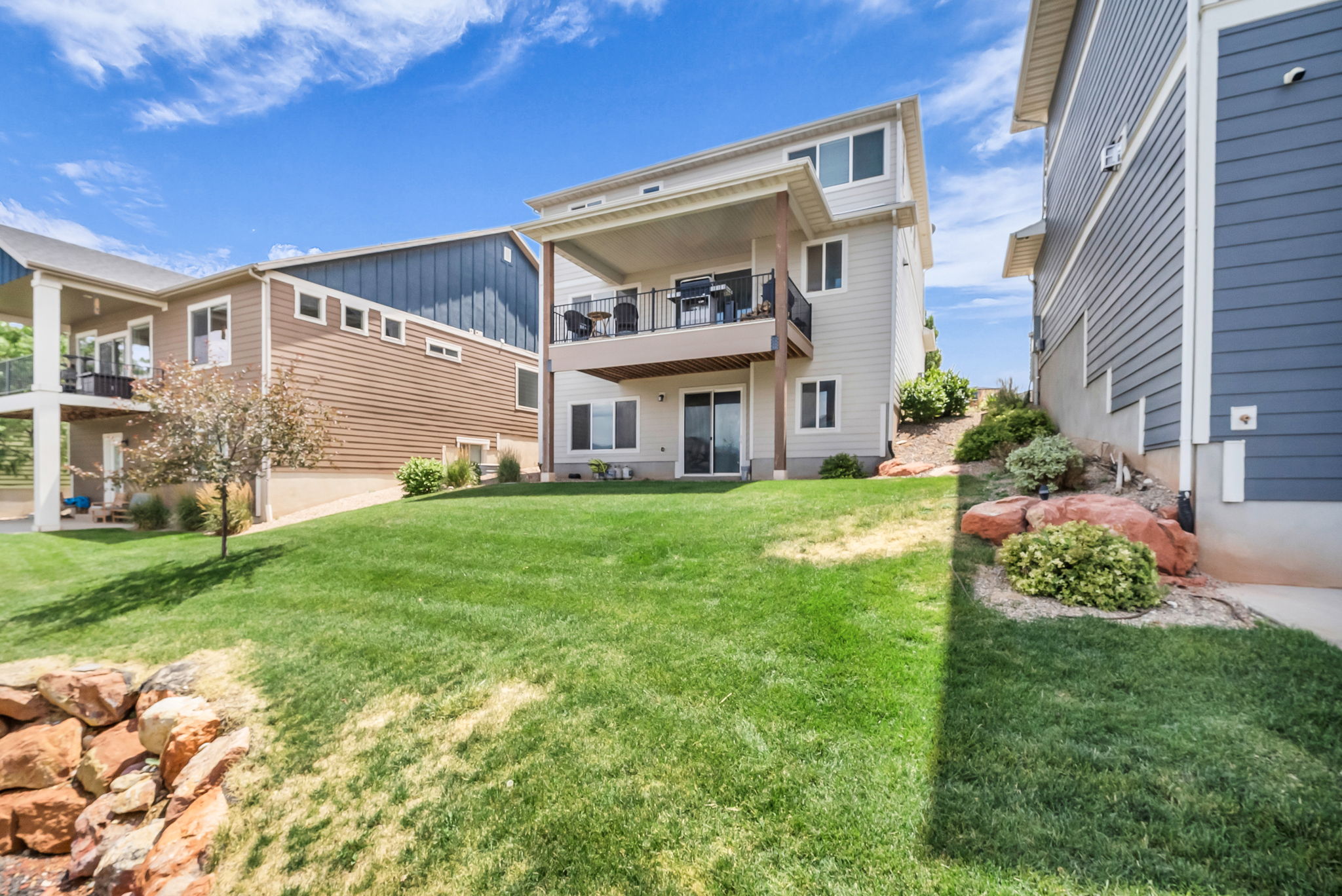Expansive backyard with a manicured lawn, an upper-level covered balcony, and a lower-level patio with sliding glass door access