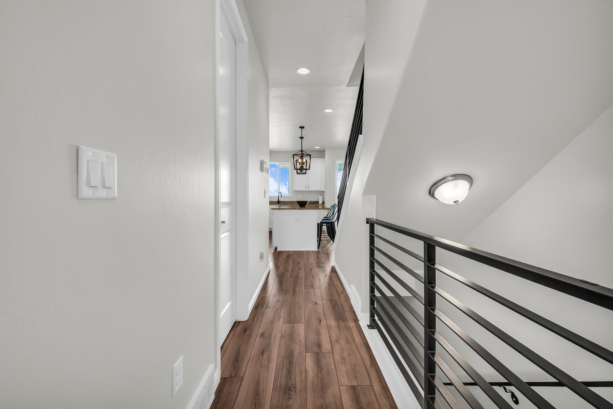 Hardwood-finish flooring extending through the hallway, leading towards a kitchen with white cabinetry and a window