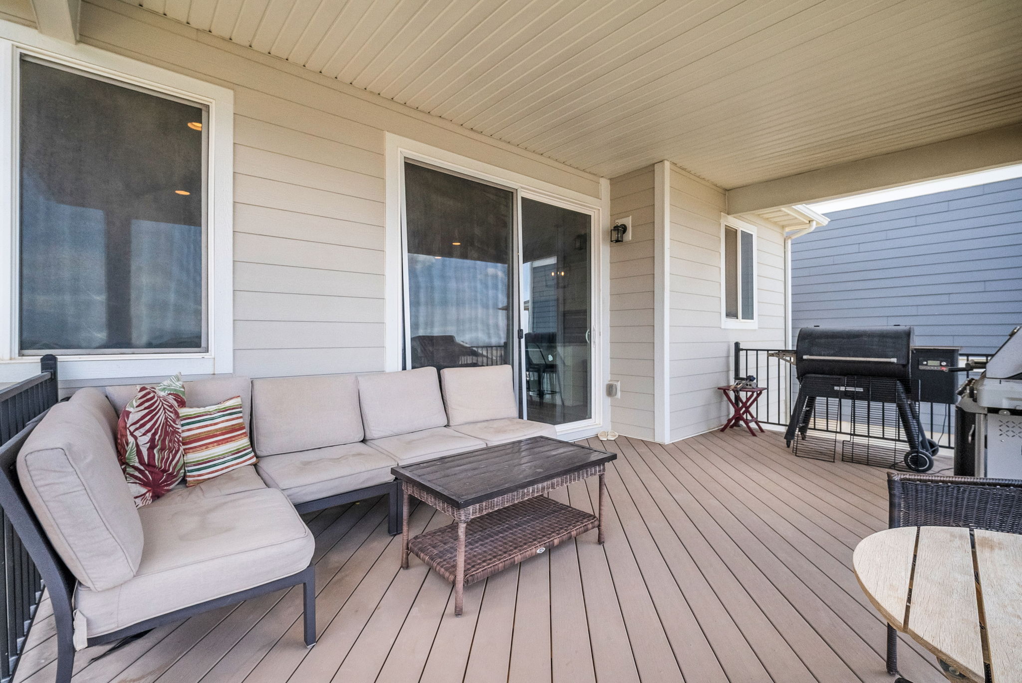 Spacious covered deck featuring composite decking, white vinyl siding, a sliding glass door, and a black metal railing