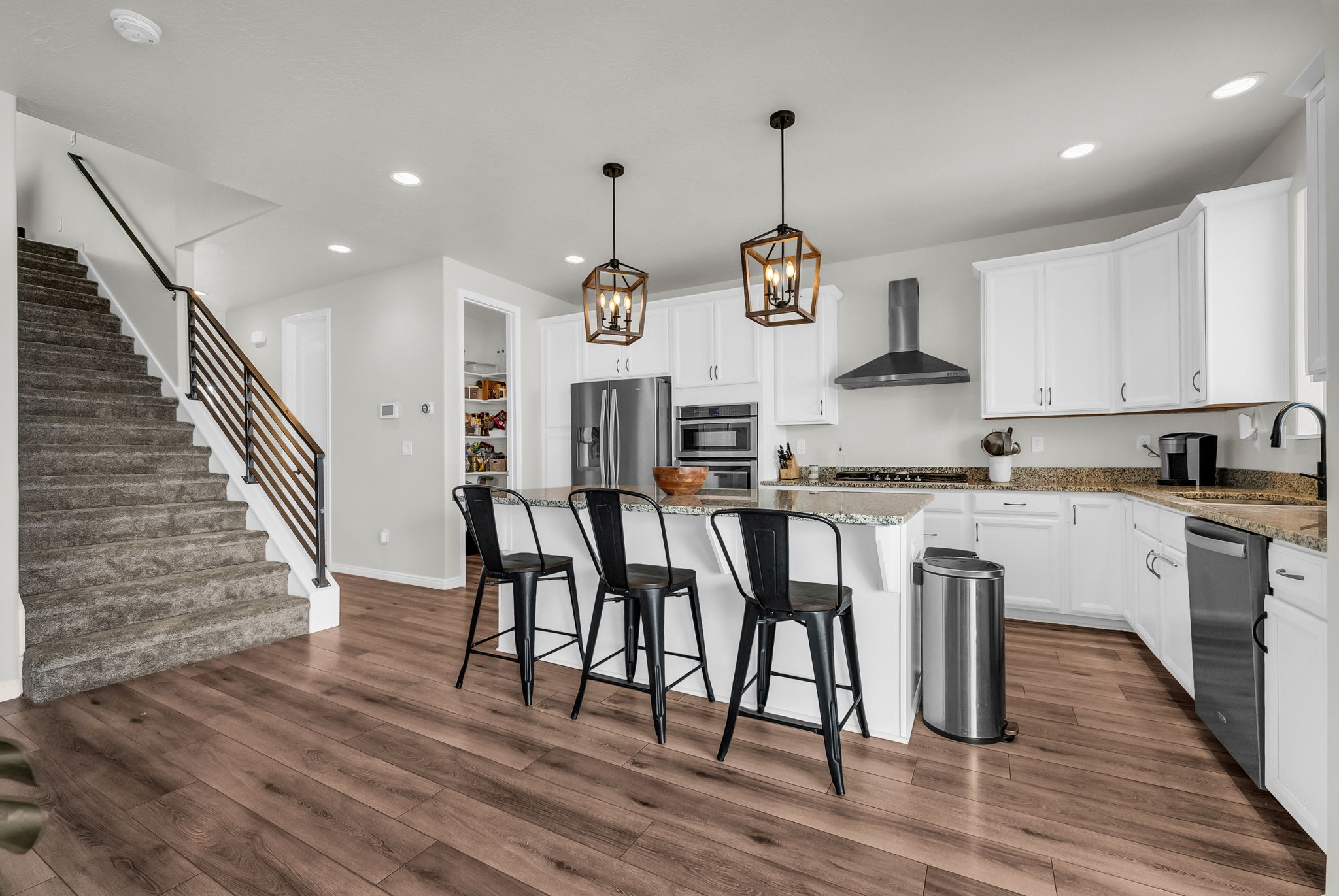 Open-concept kitchen featuring white cabinetry, stainless steel appliances, granite countertops, and a central island with pendant lighting