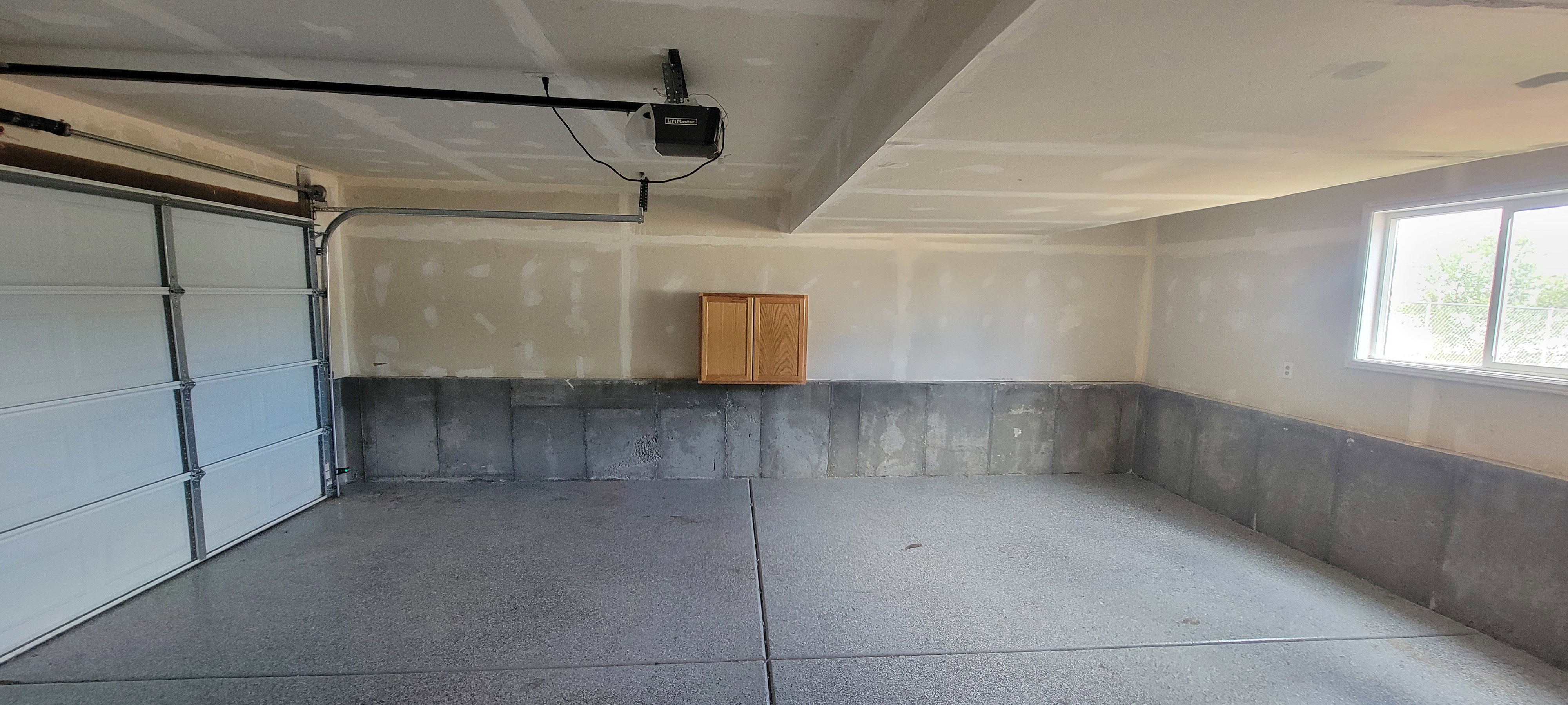 Spacious garage with epoxy-coated concrete flooring, an automatic overhead door, a built-in wood cabinet, and a window providing natural light