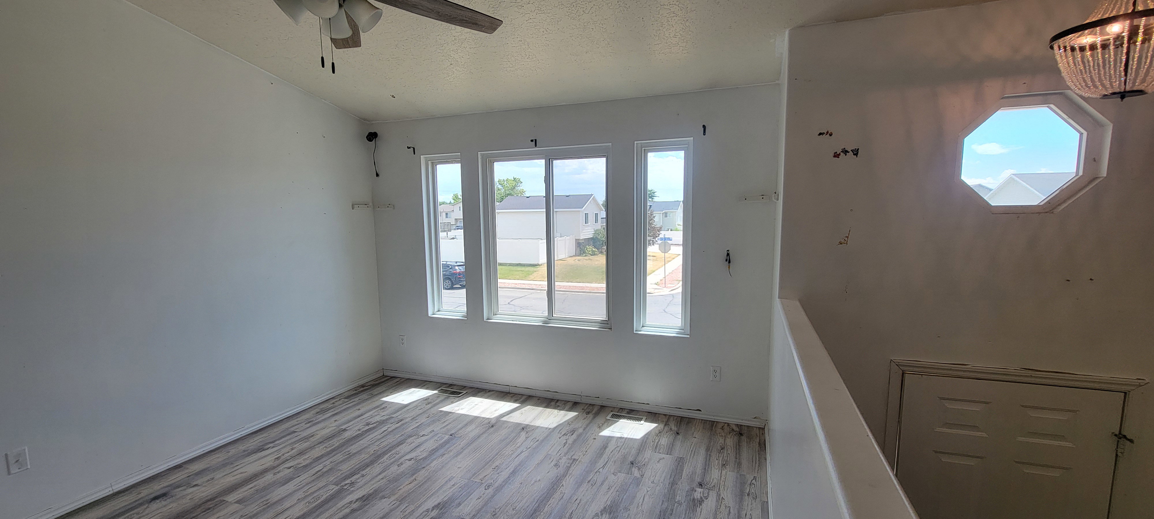 Living area featuring wood-finish flooring, three prominent windows, and a ceiling fan