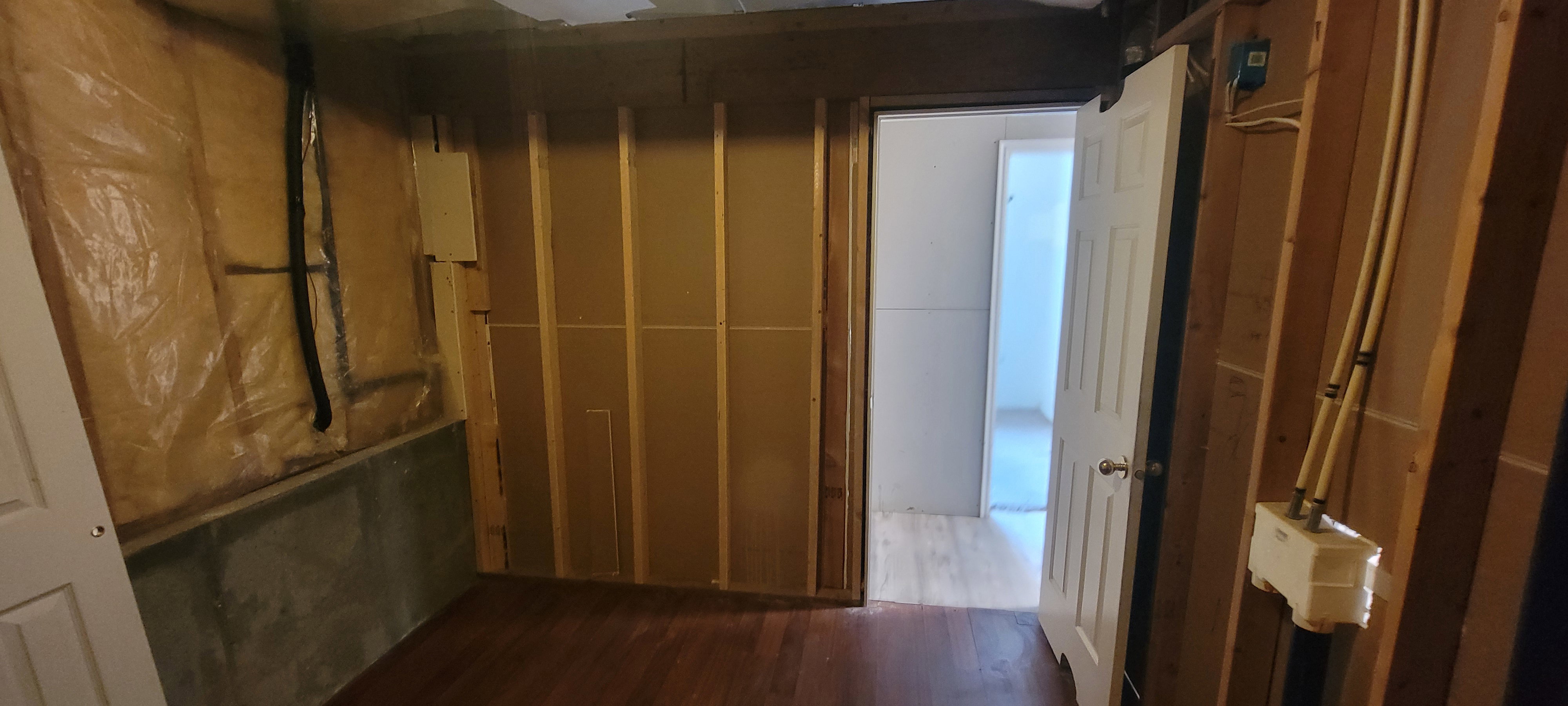 Unfinished space featuring wood-finish flooring, exposed wall studs, and visible insulation