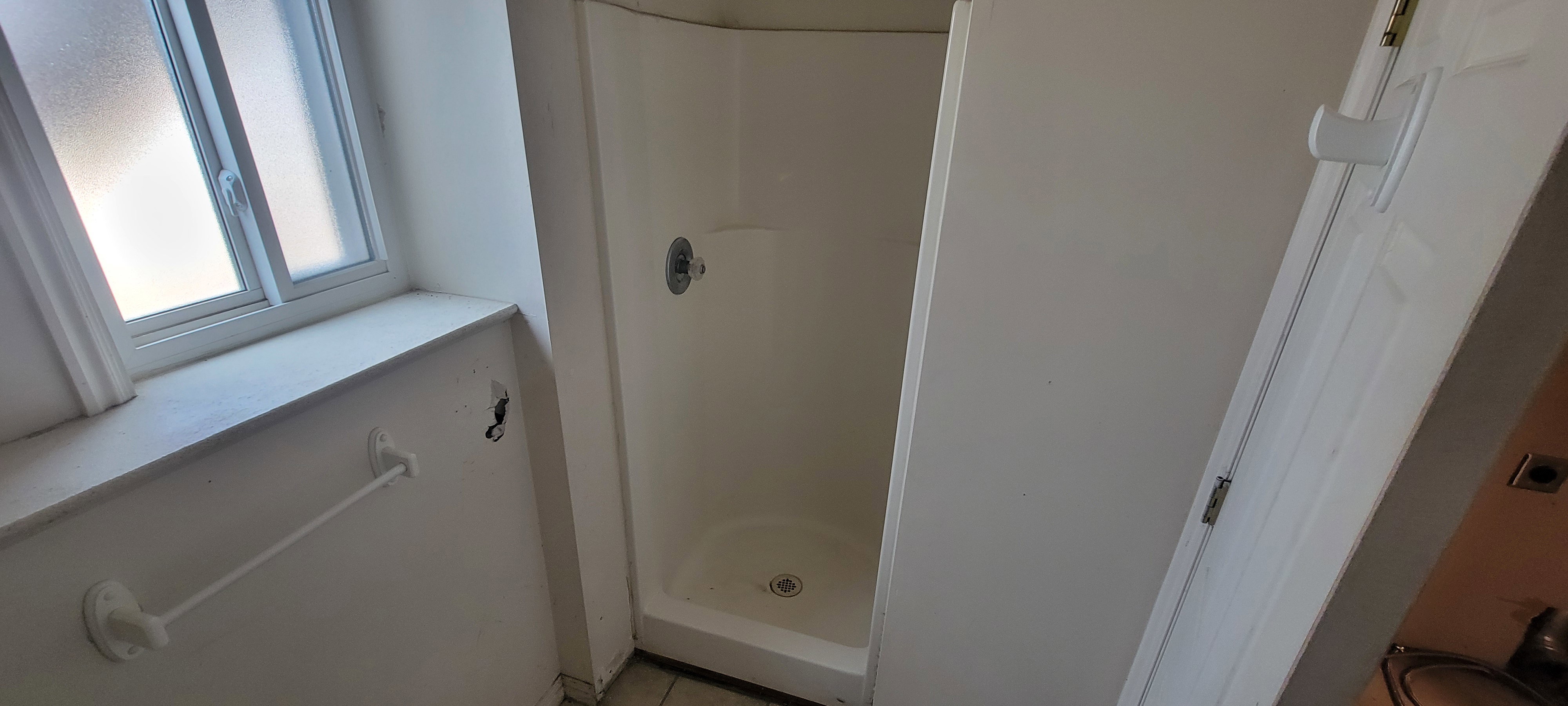 White shower stall with an integrated base, chrome shower control, and a white framed window with frosted panes