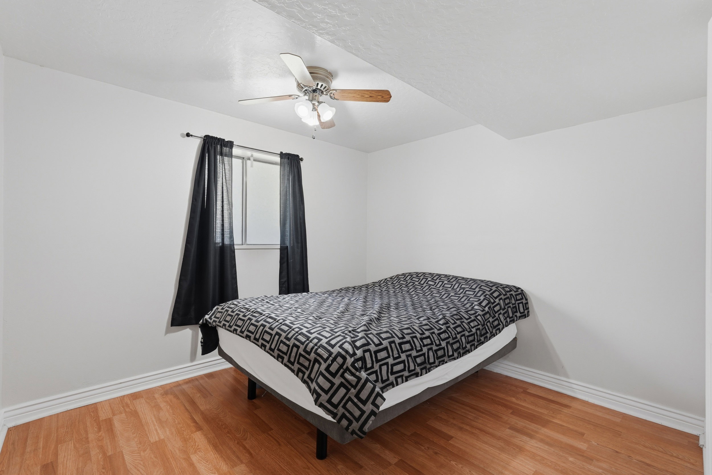 Light-filled room featuring wood-finish flooring, white baseboards, and a ceiling fan with light fixture