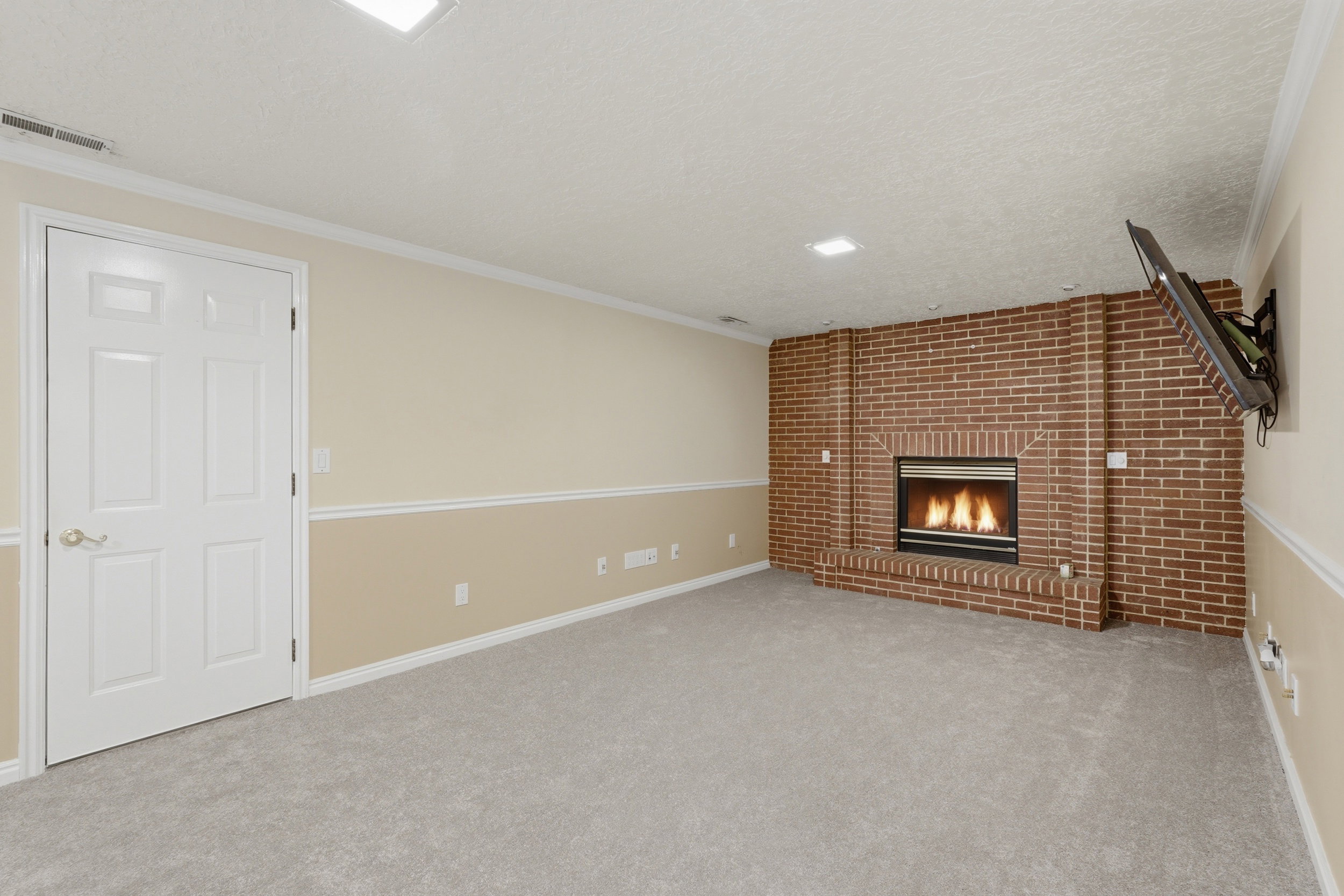 Spacious room featuring a brick fireplace, light-toned carpeting, two-tone painted walls, and recessed lighting