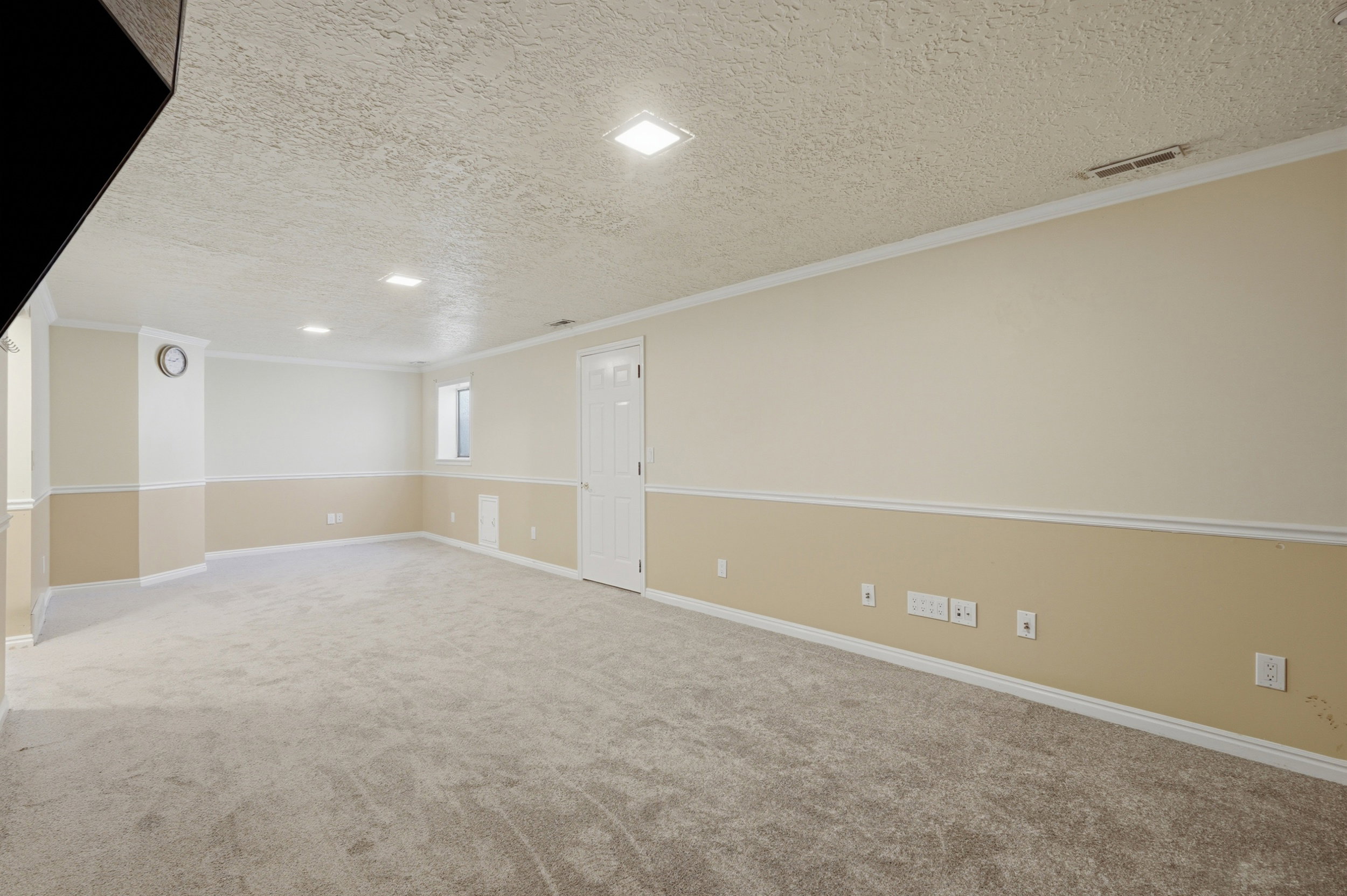 Spacious room featuring light-colored carpeting, two-tone wall paint with white trim, recessed lighting, and a white paneled door