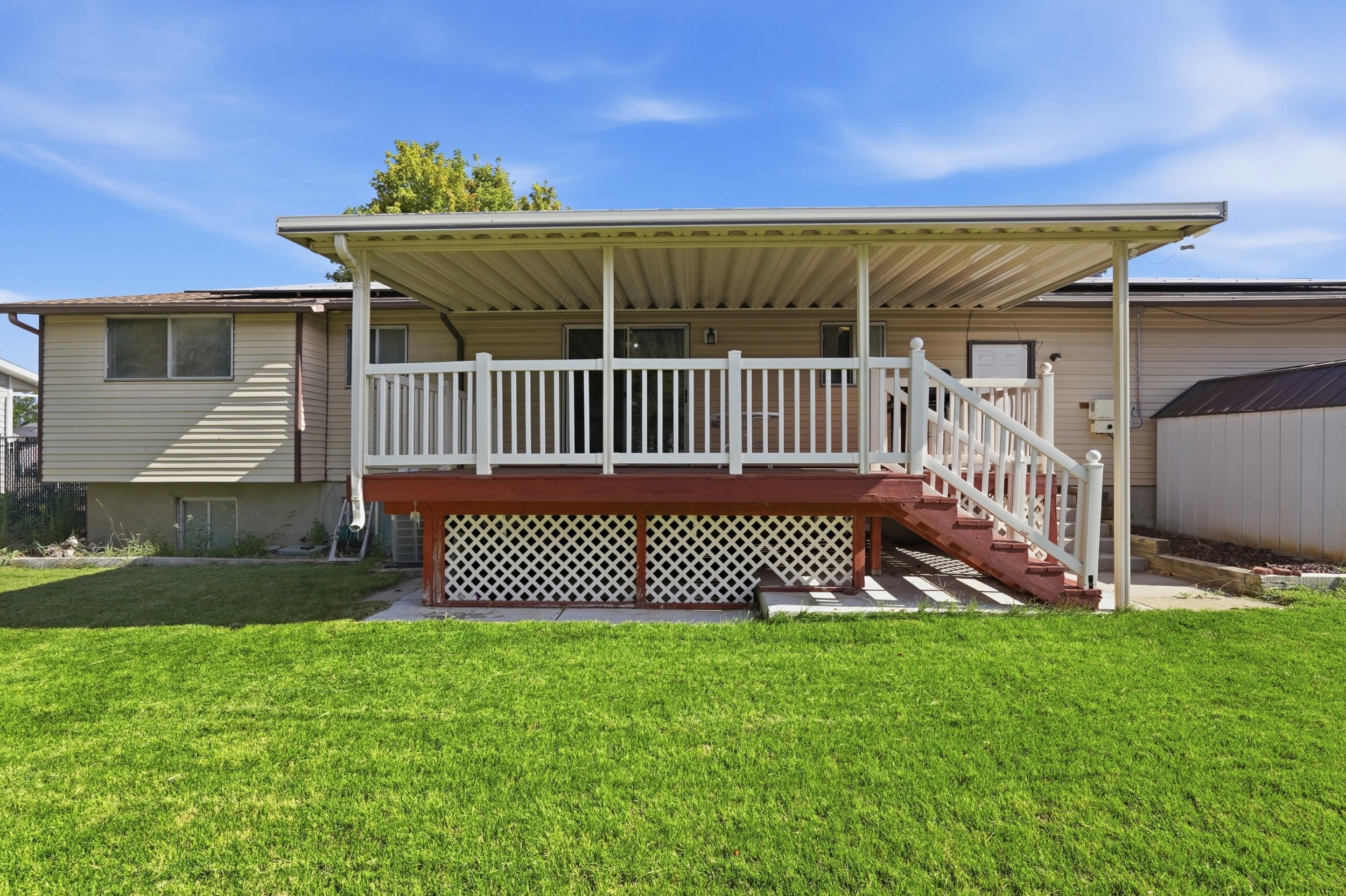 Rear exterior featuring an expansive green lawn and a covered deck