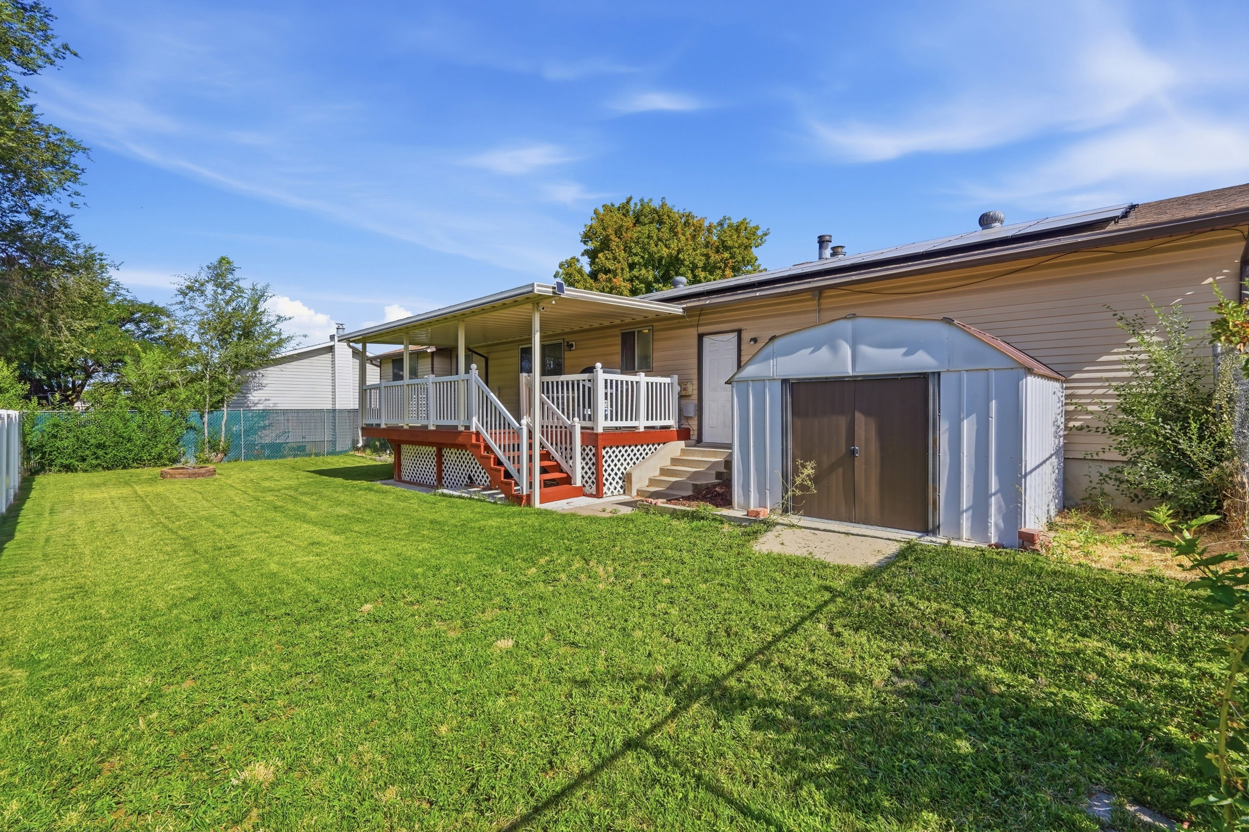 Expansive backyard featuring a covered deck with white railings, a detached storage shed, and a green lawn