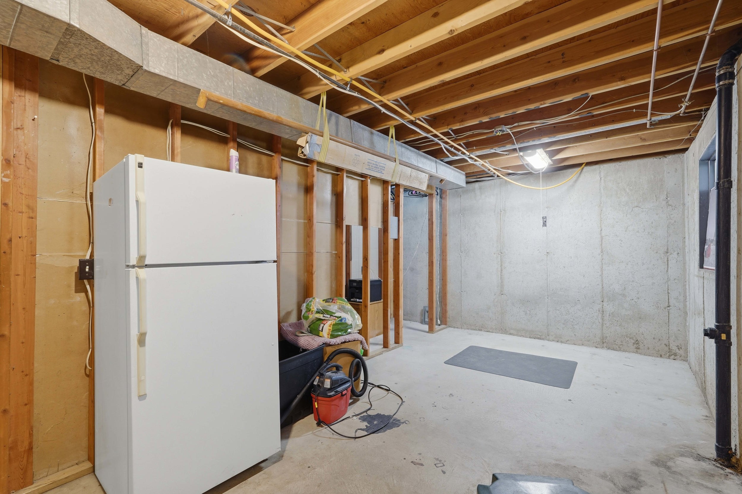 Unfinished basement with exposed wood framing, concrete foundation walls, a concrete floor, and visible overhead utilities