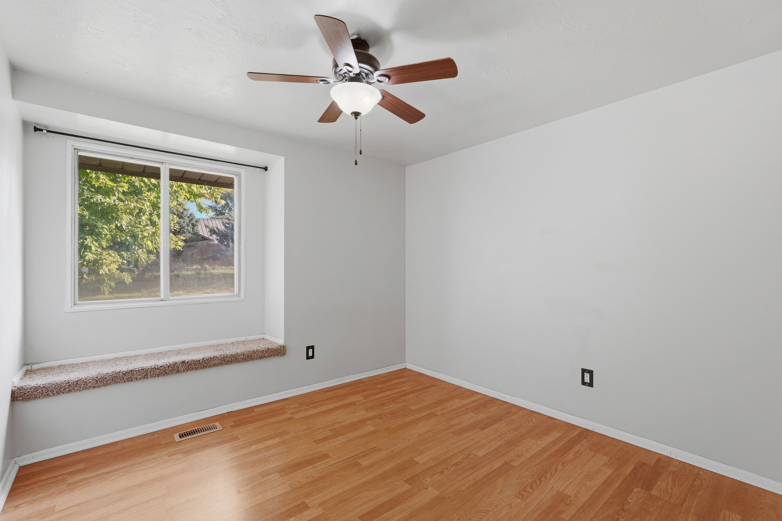 Room featuring a window with a carpeted sill, wood-finish flooring, white walls, and a ceiling fan with light fixture