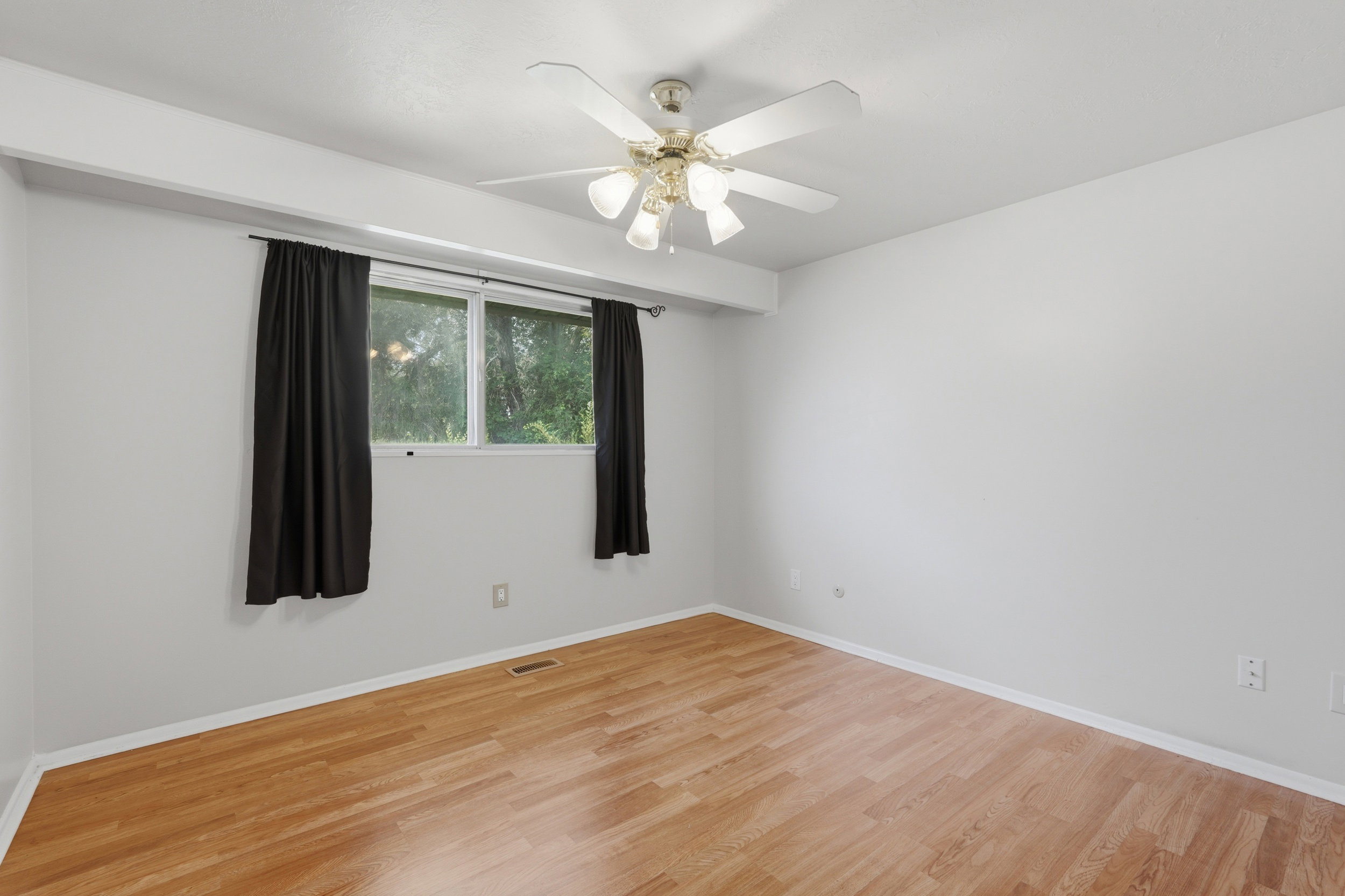 Spacious room featuring wood-finish flooring, a ceiling fan with integrated lighting, and a large window