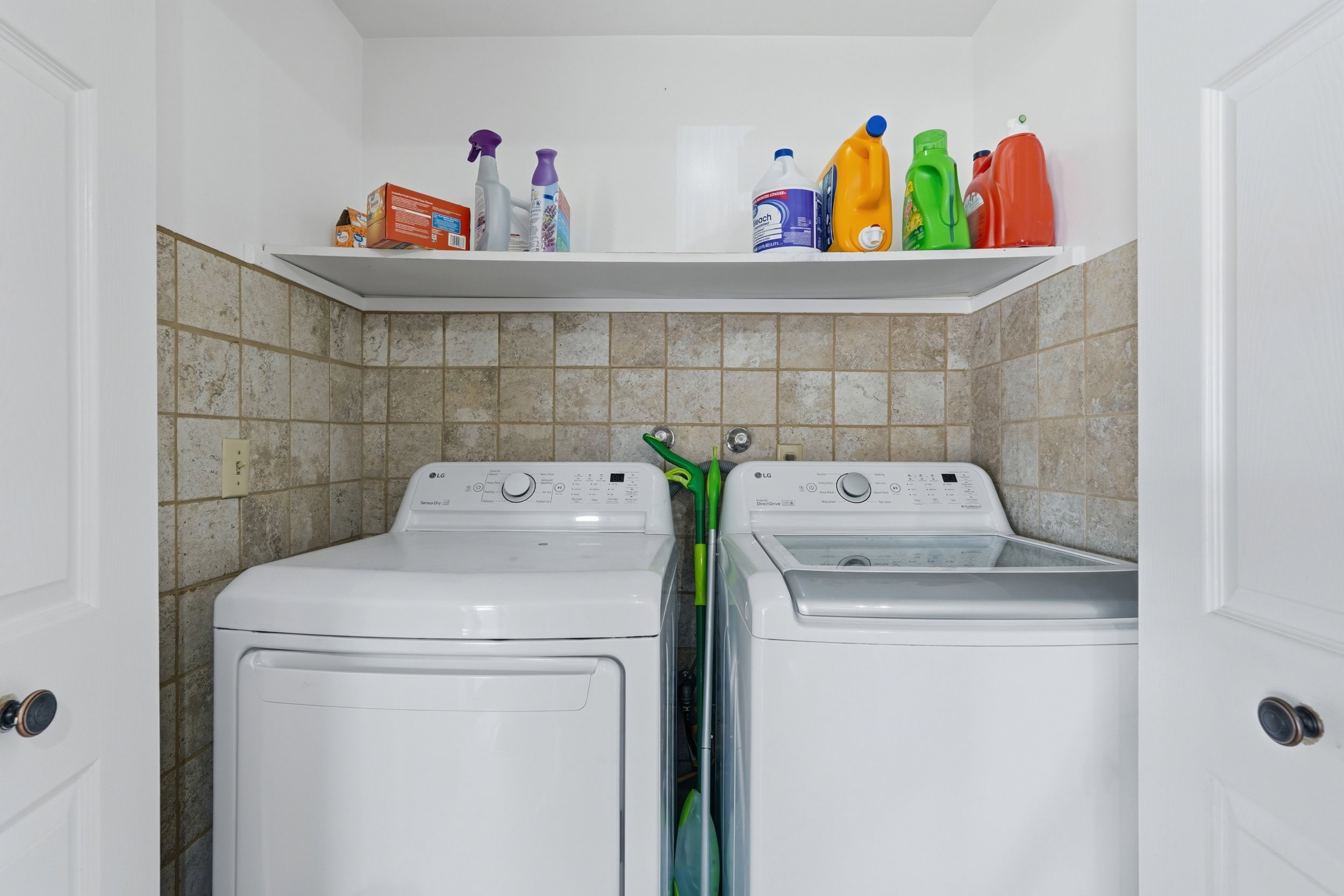 Dedicated laundry area featuring a tiled wall backsplash and an overhead storage shelf