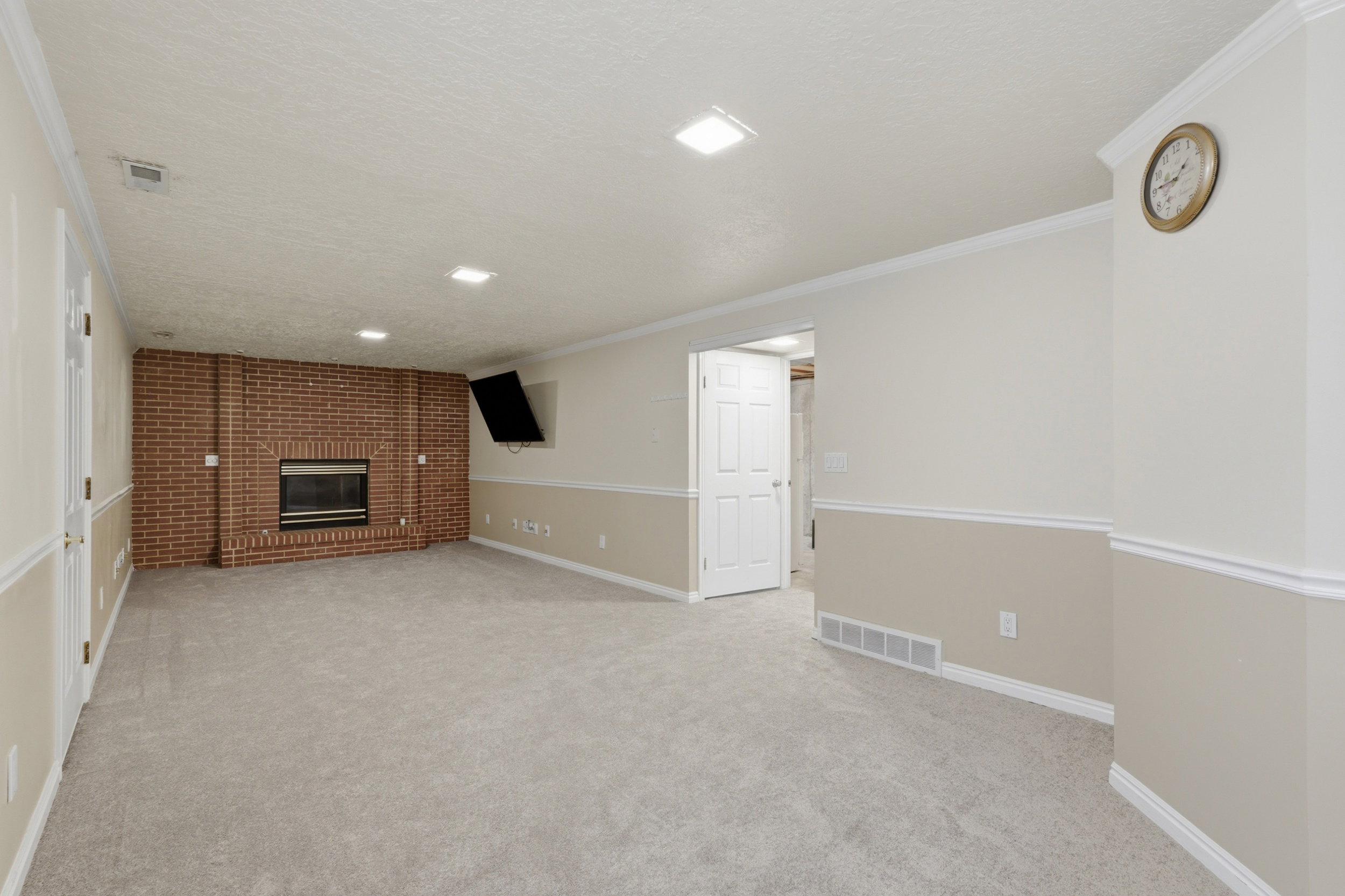 Spacious room featuring a brick fireplace with a black insert, light gray carpet, and two-tone wall paint with white wainscoting