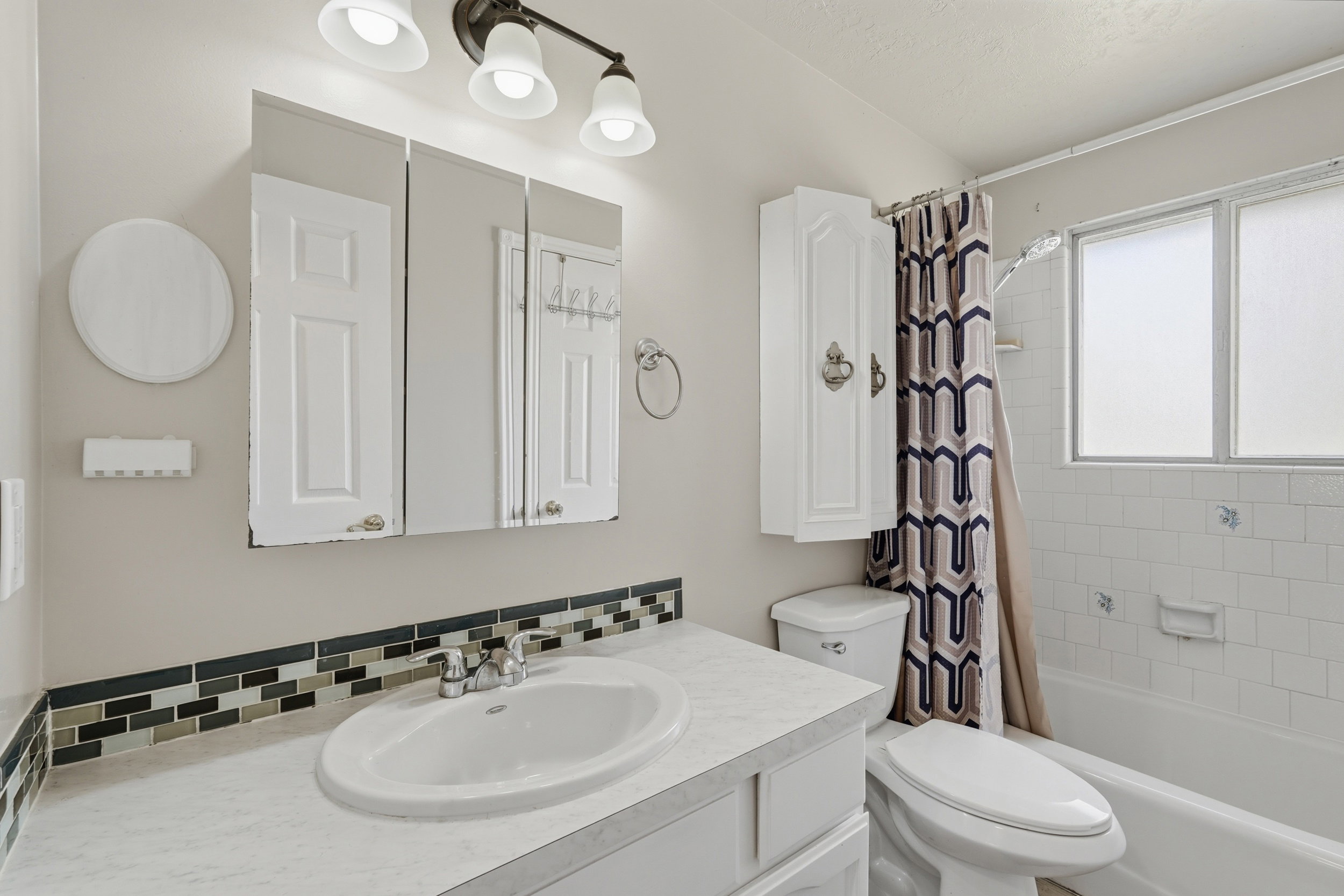 Bathroom featuring a vanity with an integrated sink, a three-door mirrored medicine cabinet, and a multi-light fixture