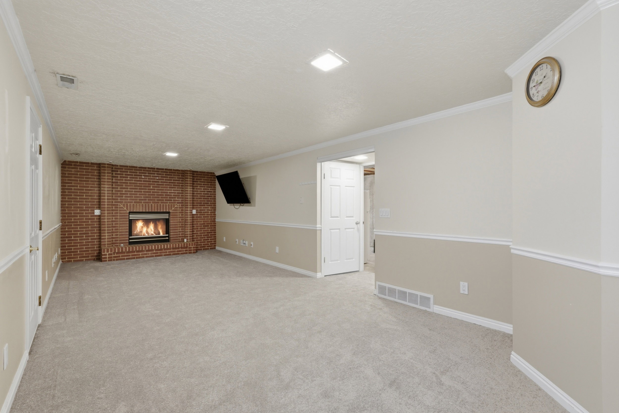 Spacious room featuring a brick fireplace with a glass front, light gray carpeting, two-tone painted walls with chair rail molding, recessed lighting, and white trim throughout