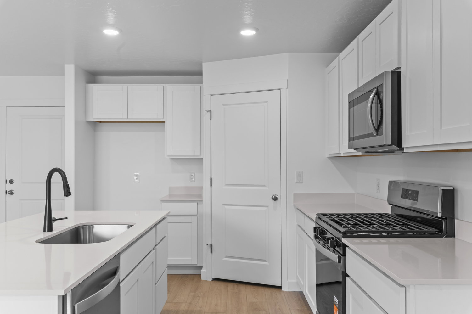 Modern kitchen featuring white cabinetry, light countertops, a stainless steel gas range, a built-in microwave, and an island with an undermount sink and black faucet
