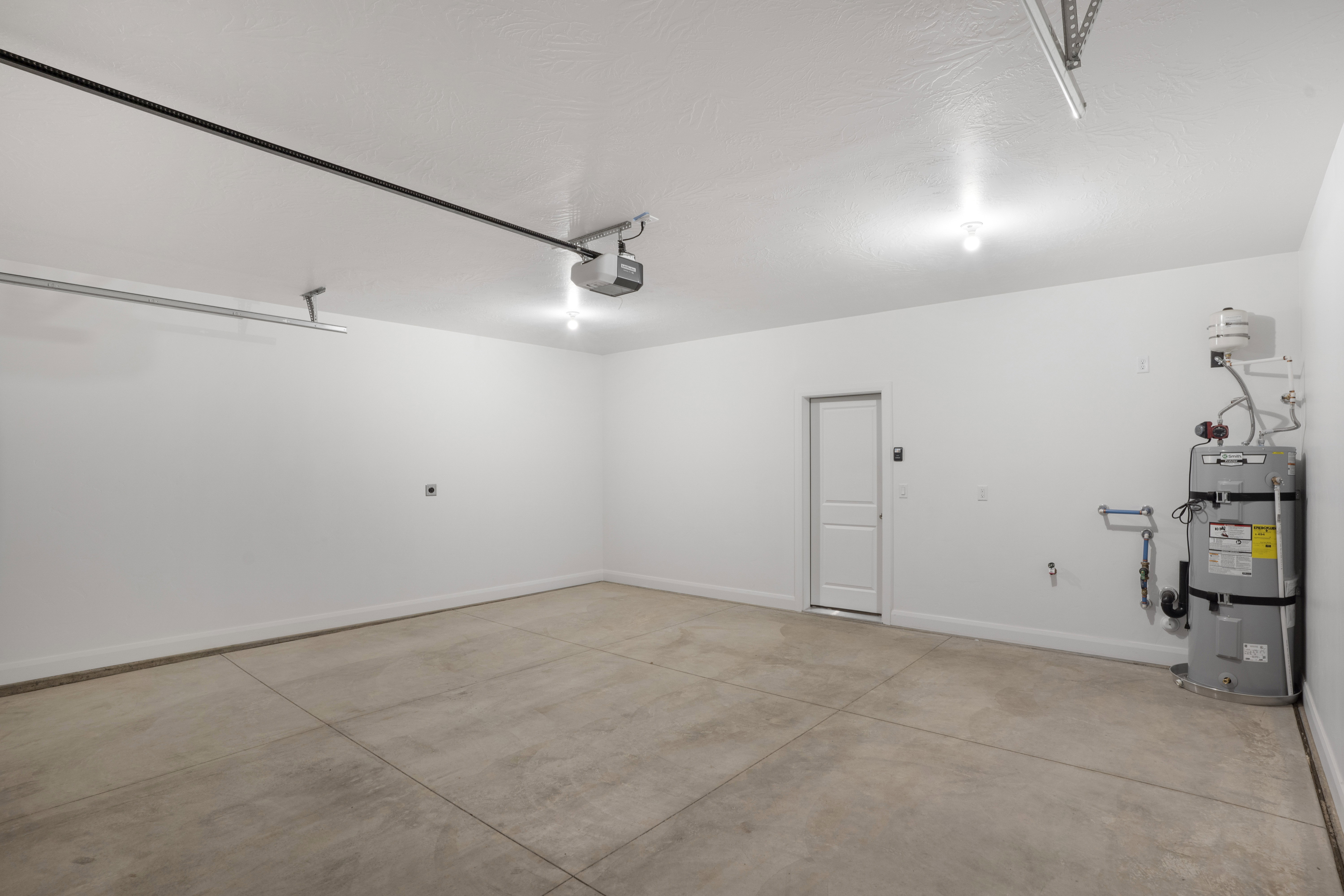 Spacious garage featuring a concrete floor, bright overhead lighting, water heater installation, and a pedestrian door for interior access