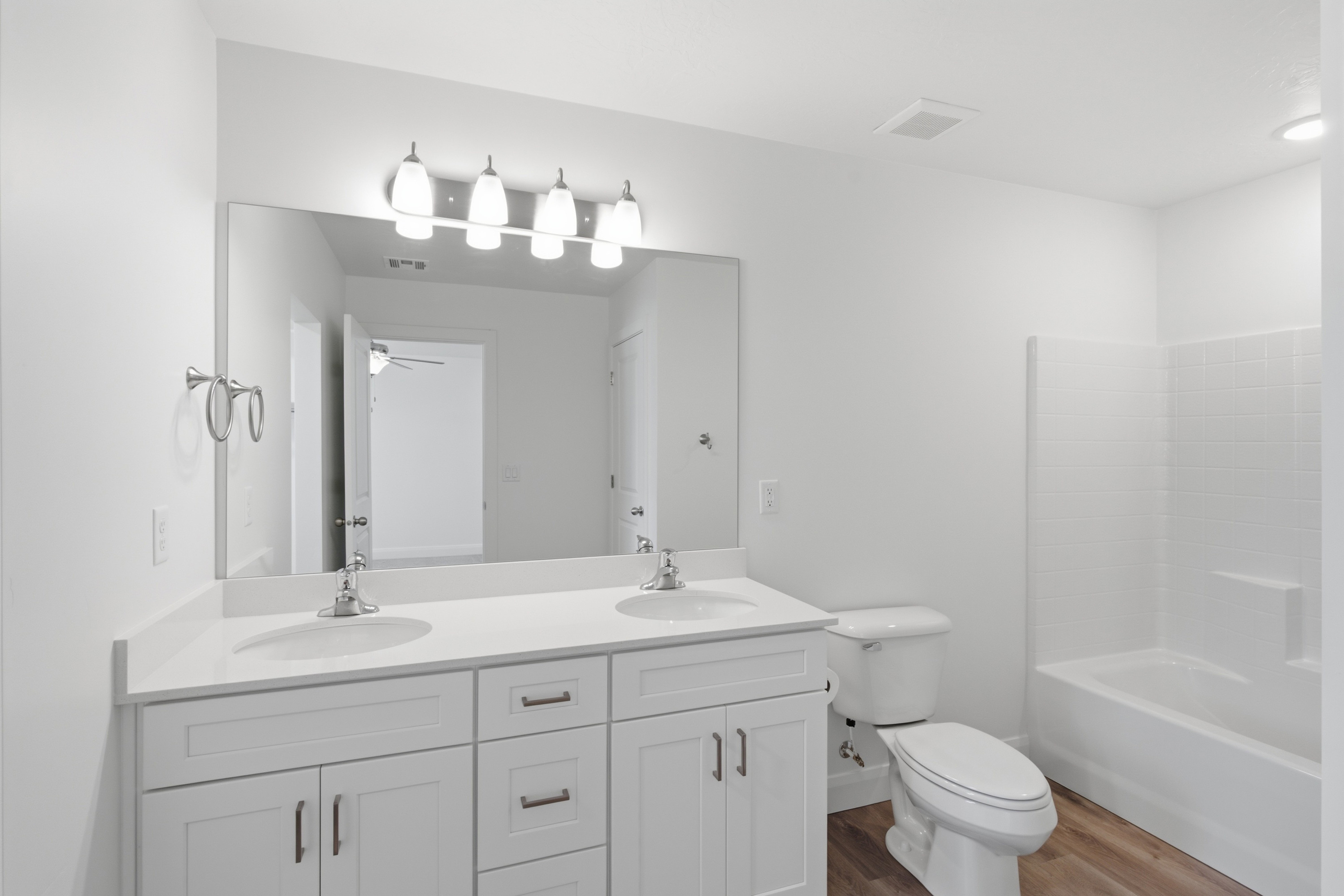 Bathroom featuring a double vanity with white cabinetry, dual undermount sinks, and a large mirror with contemporary light fixtures