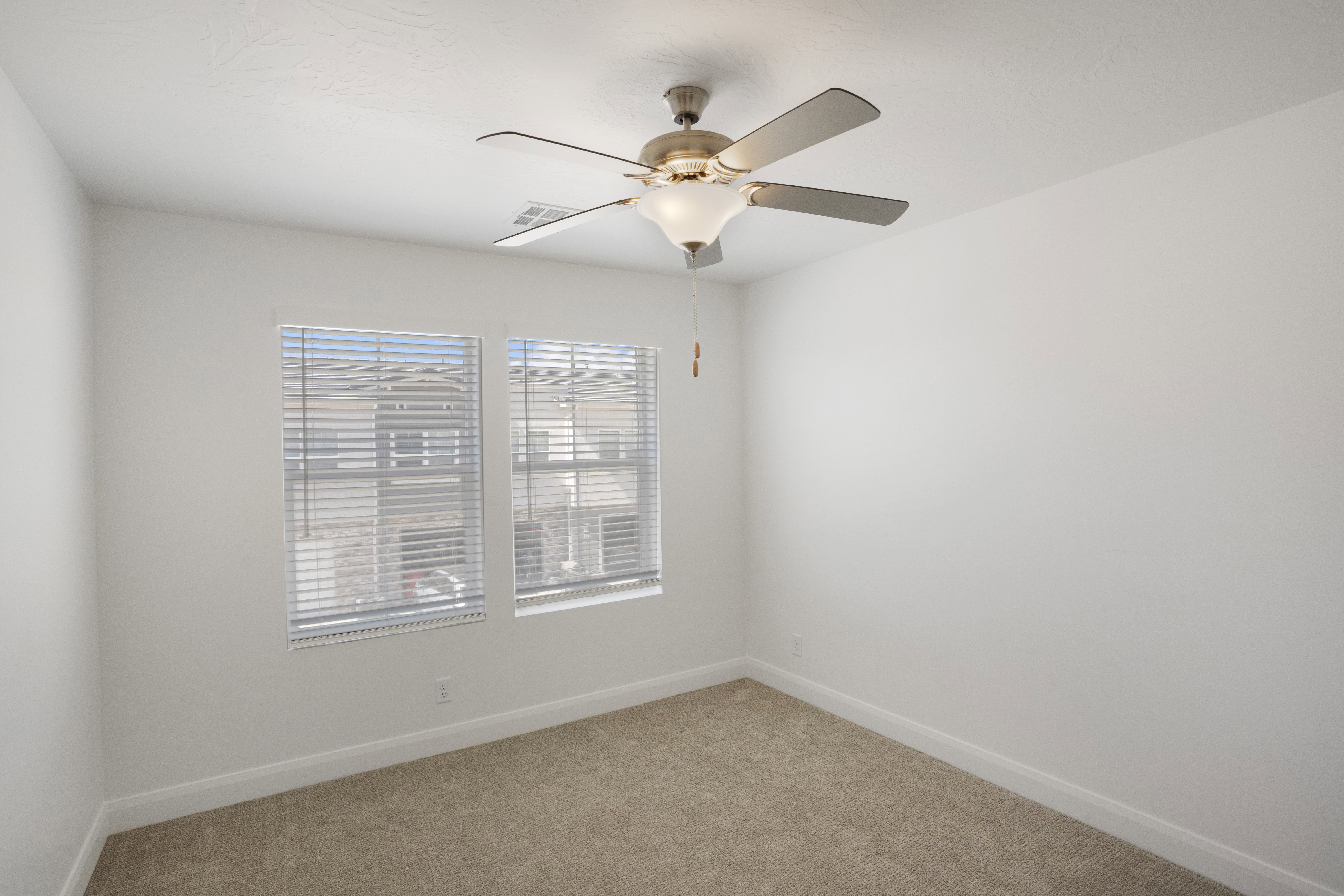 Room featuring two windows with horizontal blinds, neutral carpet flooring, white walls, and a ceiling fan with integrated lighting