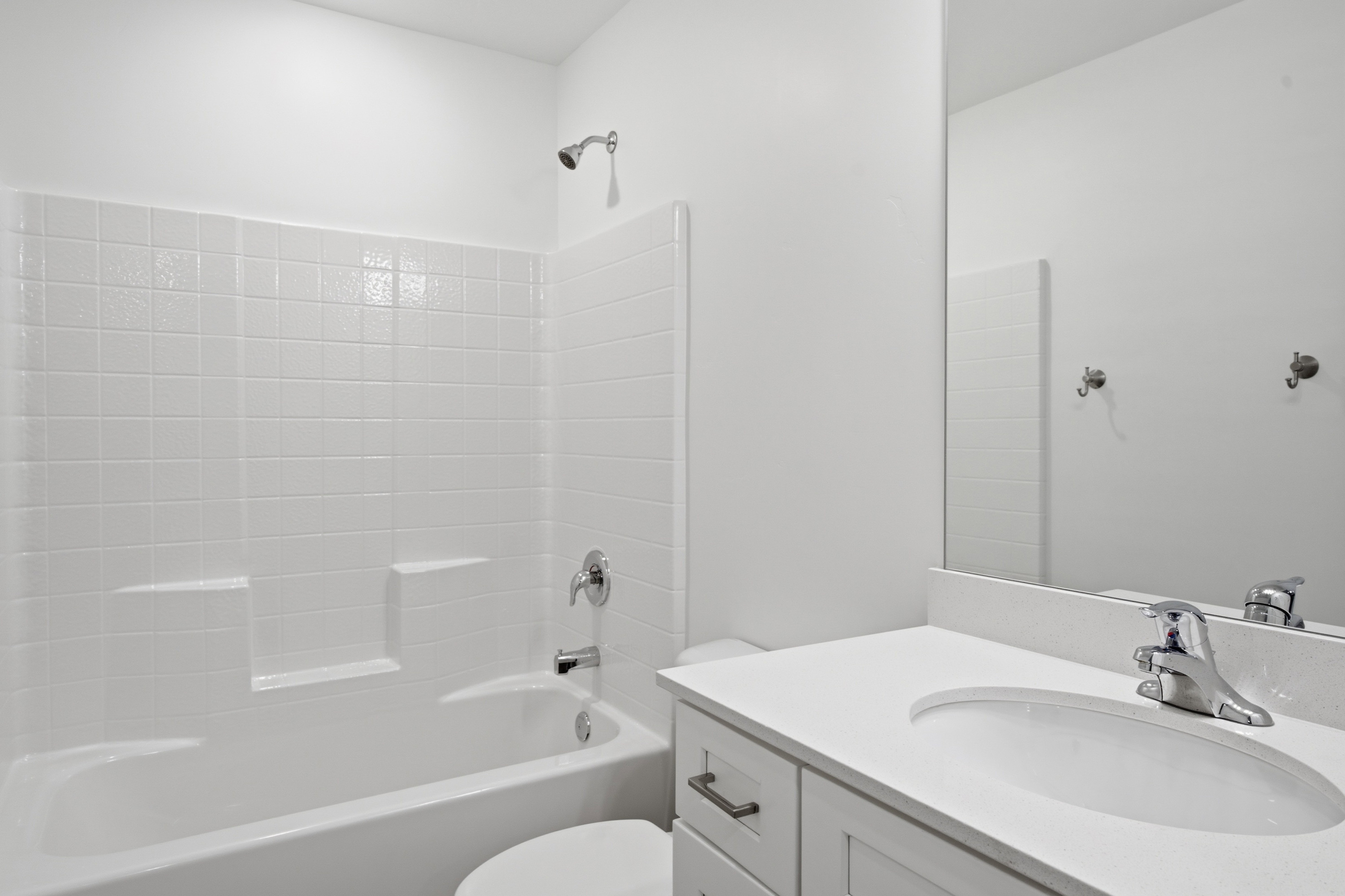 Bathroom featuring a white subway tile shower surround, a built-in tub with chrome fixtures, a vanity with a white countertop and integrated sink, and an unframed wall mirror