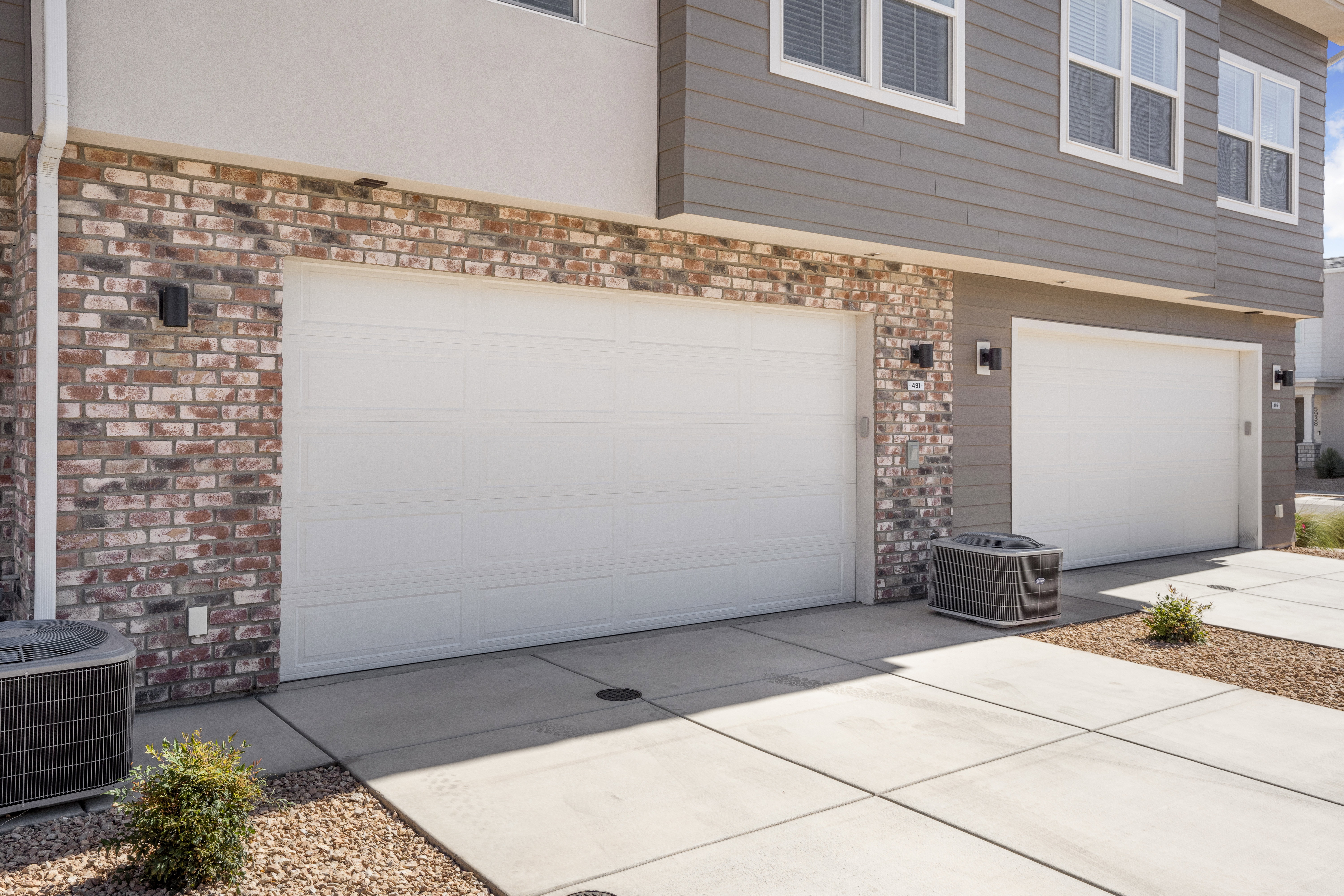 Exterior featuring two white garage doors, brick accent columns, and horizontal siding